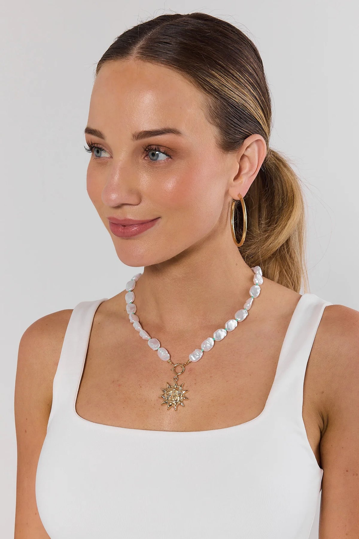 Woman wearing pearl sun charm necklace with gold pendant on white tank top - On Model | Avara