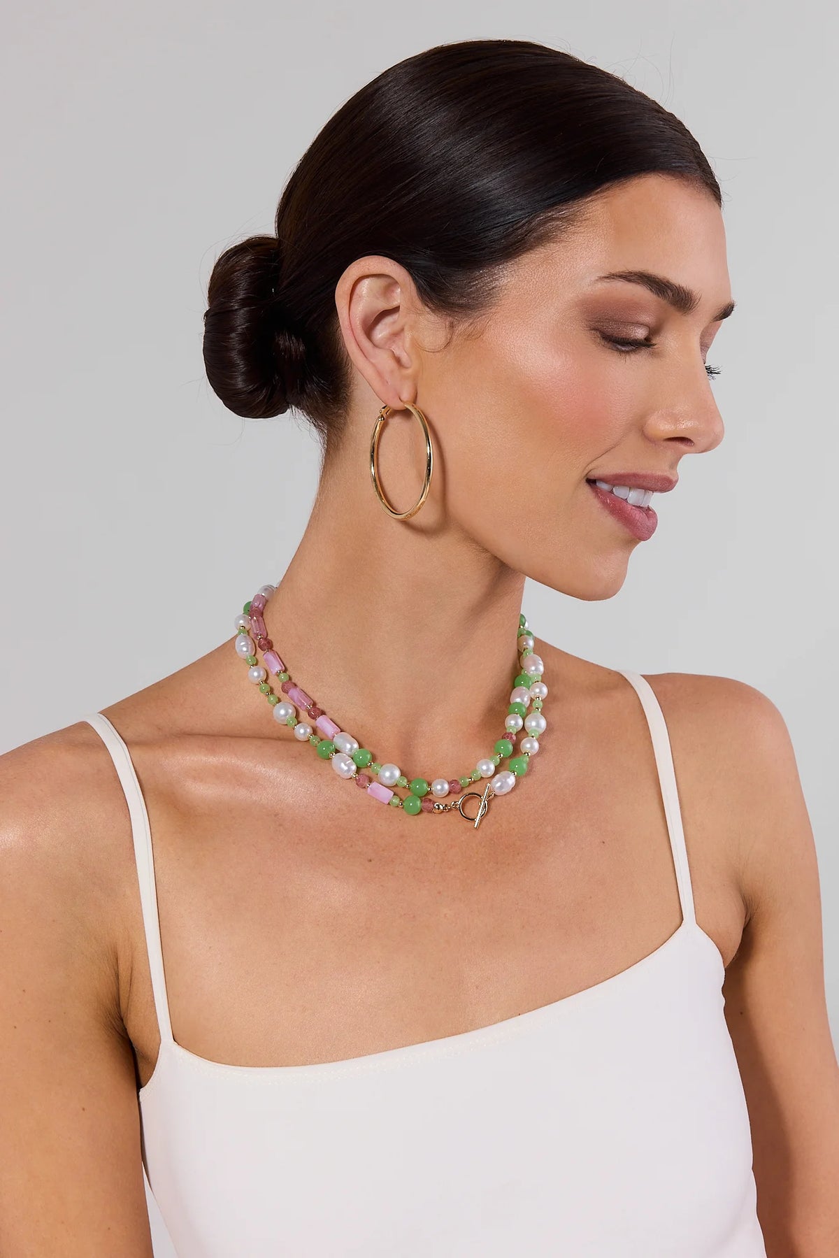 Woman wearing a colorful beaded necklace and gold hoop earrings against a plain background