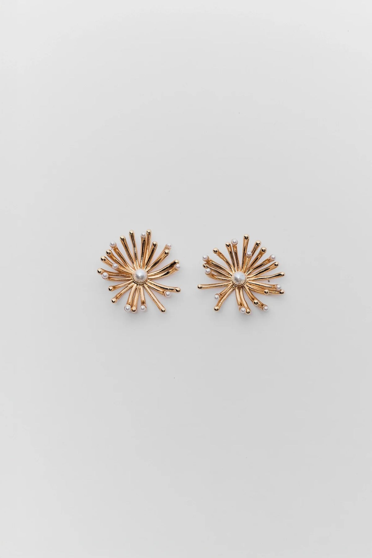 Pair of gold starburst earrings on a light gray background