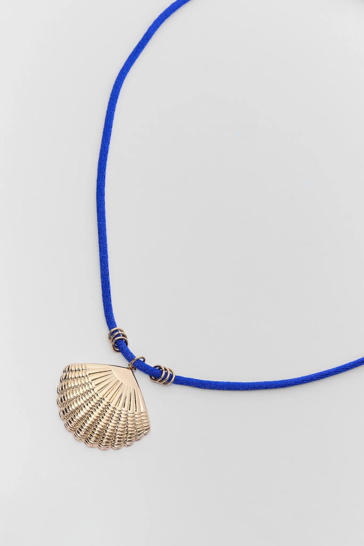 Close-up of gold shell charm pendant on blue cord necklace showing hardware detail | Avara