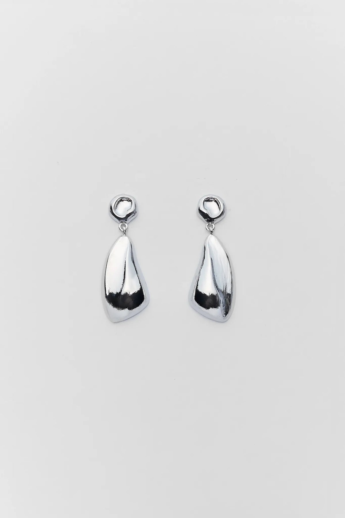 Pair of polished silver abstract drop earrings on light gray background - Flat Lay | Avara