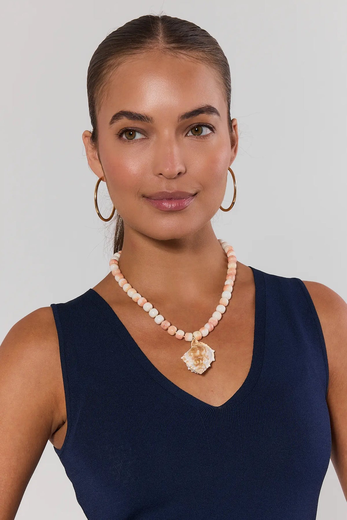 Woman wearing a necklace with a large pendant against a plain background