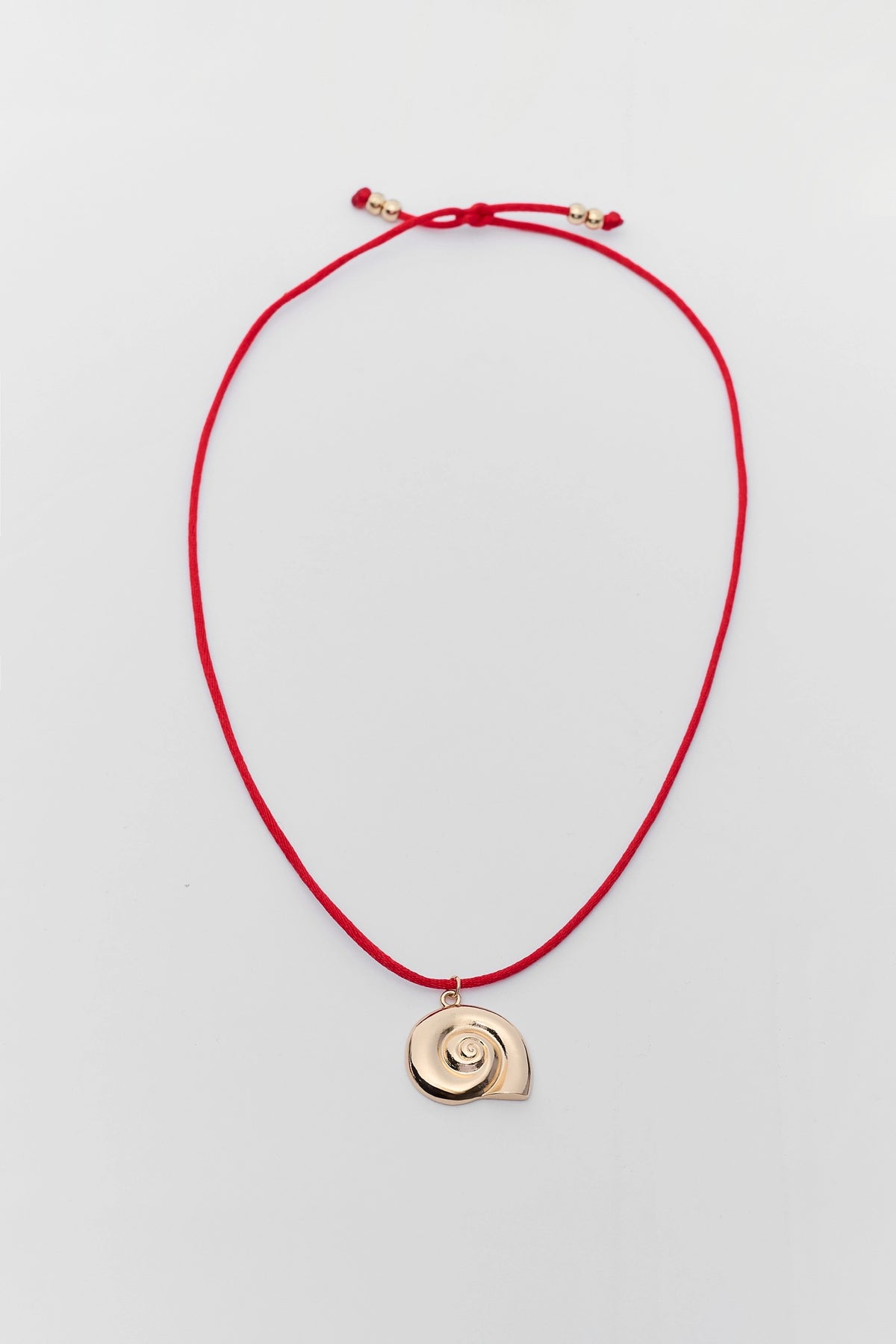 Red cord shell charm necklace with gold spiral snail pendant and adjustable beaded closure - Flat Lay | Avara