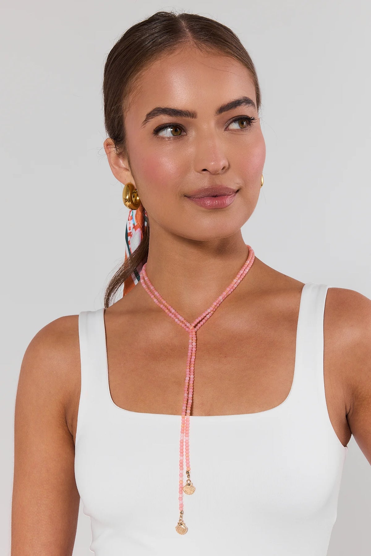 Woman wearing pink beaded wrap necklace styled as lariat with gold shell charms, white tank top - On Model | Avara