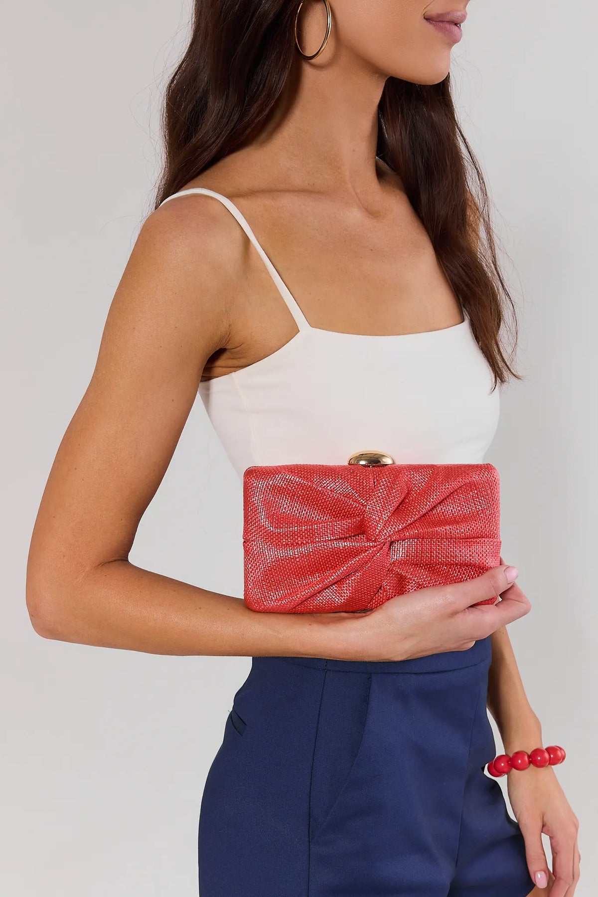 Woman holding pink textured knotted clutch bag with gold hinge closure - On Model Detail | Avara