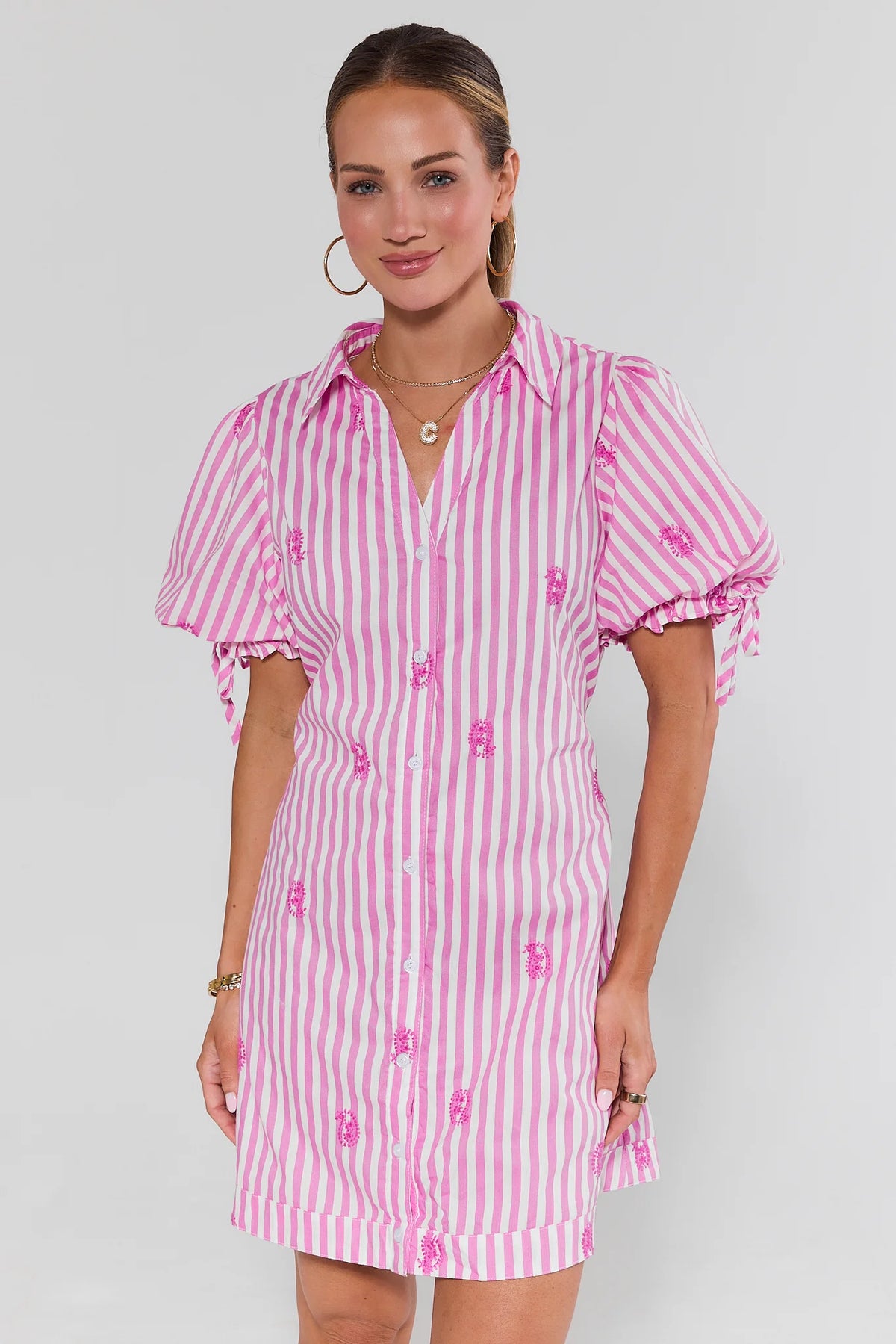 Woman wearing a pink and white striped dress with puff sleeves on a plain background