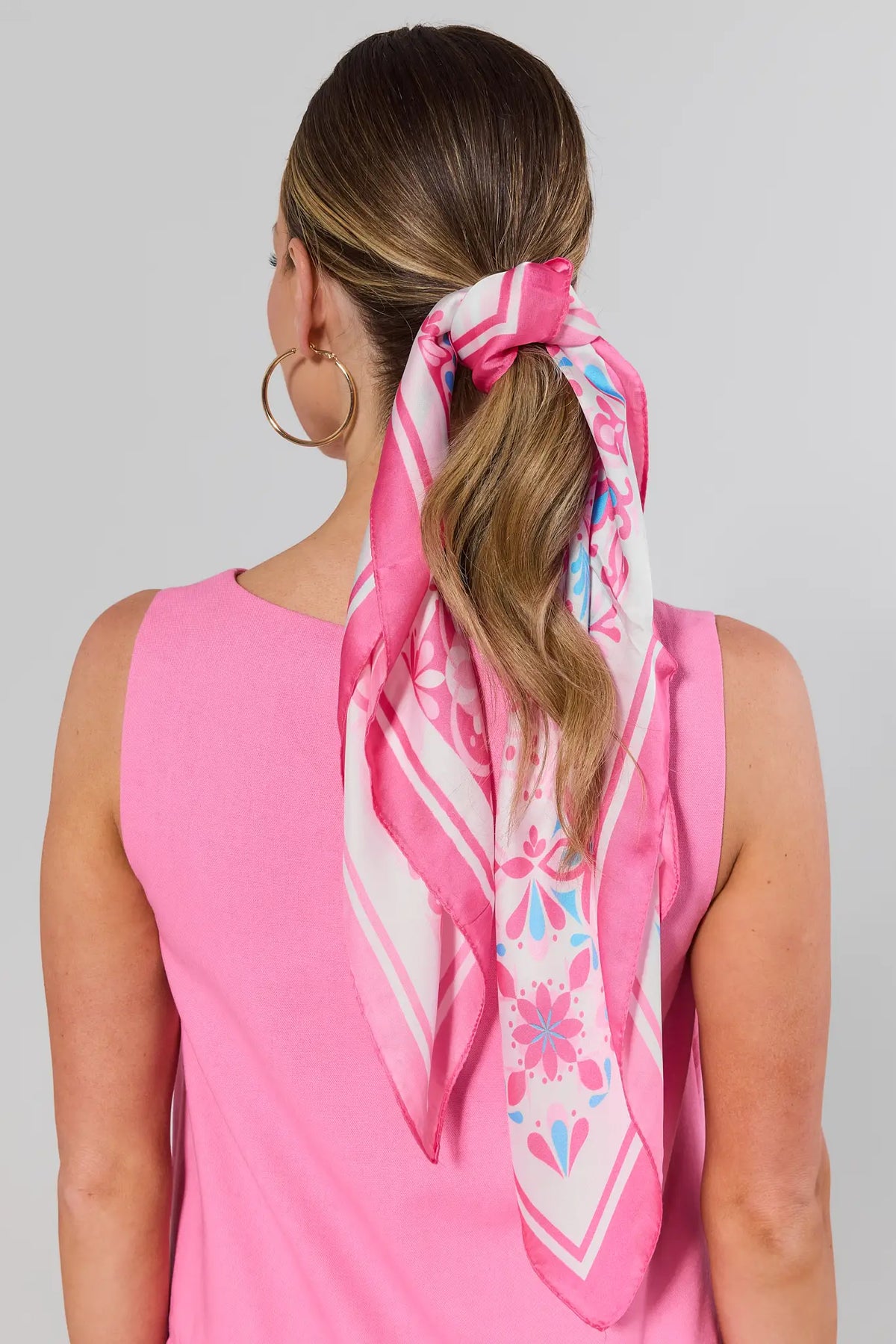 Woman wearing a pink floral scarf tied around her hair with a plain background