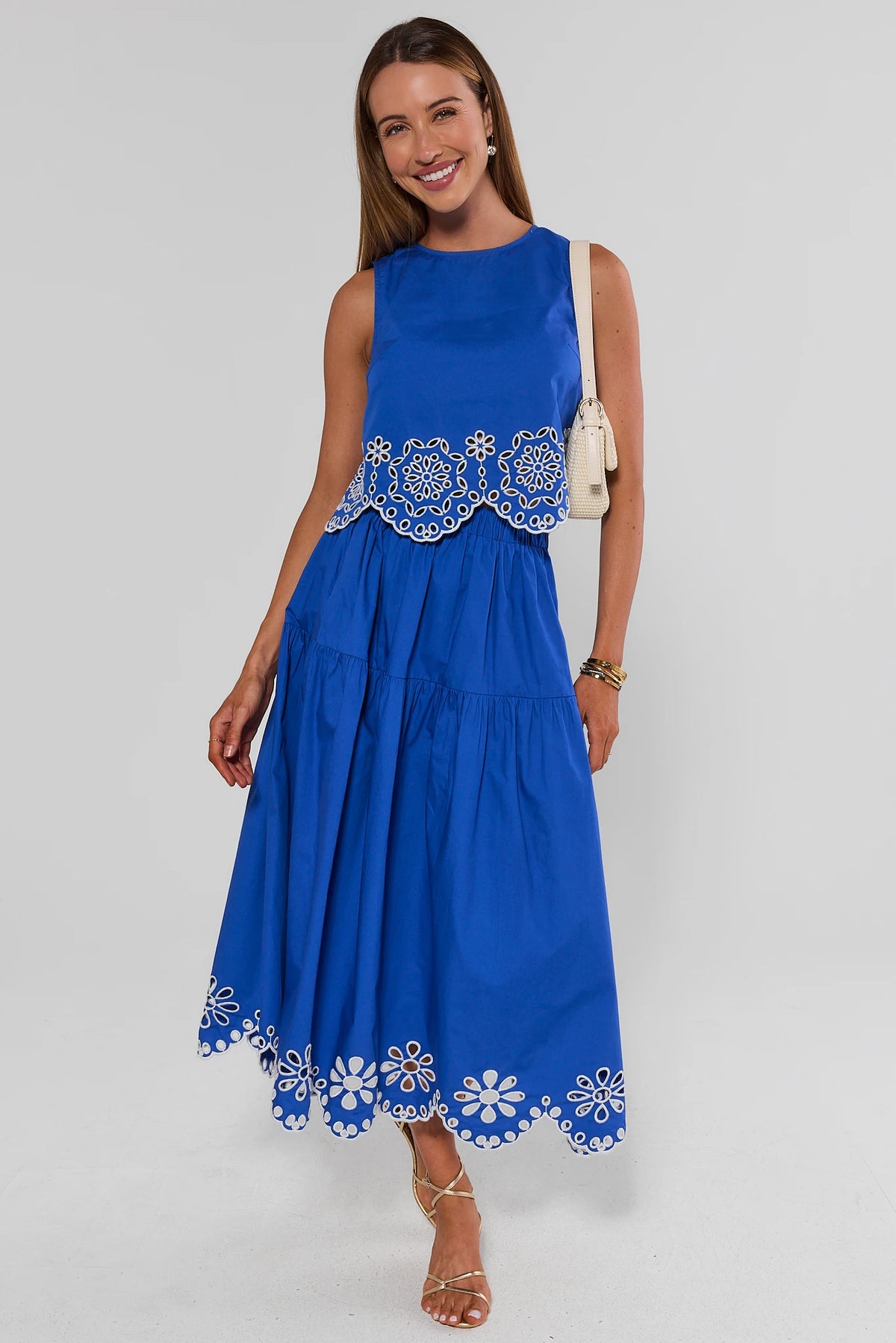 Woman wearing a blue dress with white floral embroidery on a gray background stand