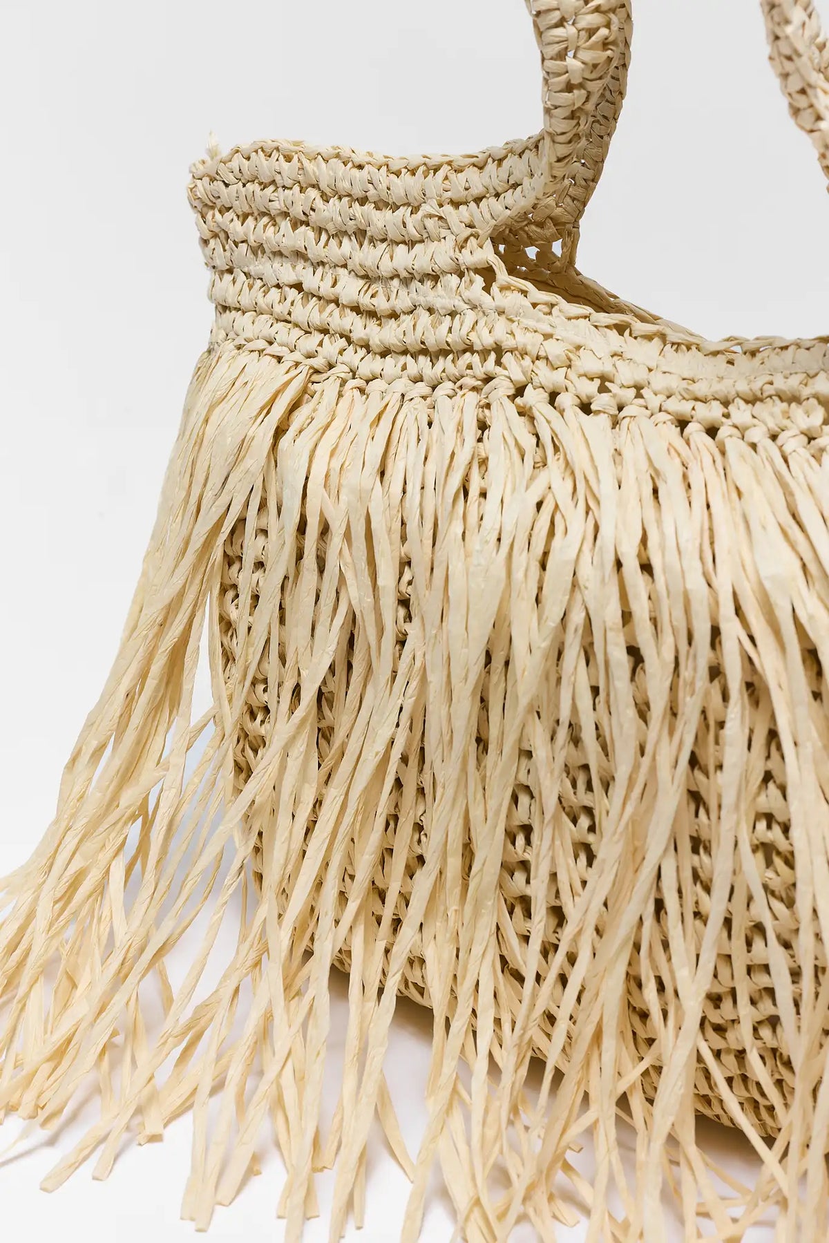 Close-up of tan woven raffia fringe bag showing fringe and weave texture detail | Avara