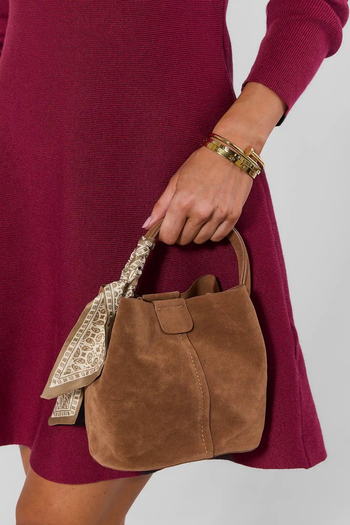 Tan Faux Suede Bag Held by Model in Burgundy Sweater Dress with Gold Bangles - Styled Look | Avara