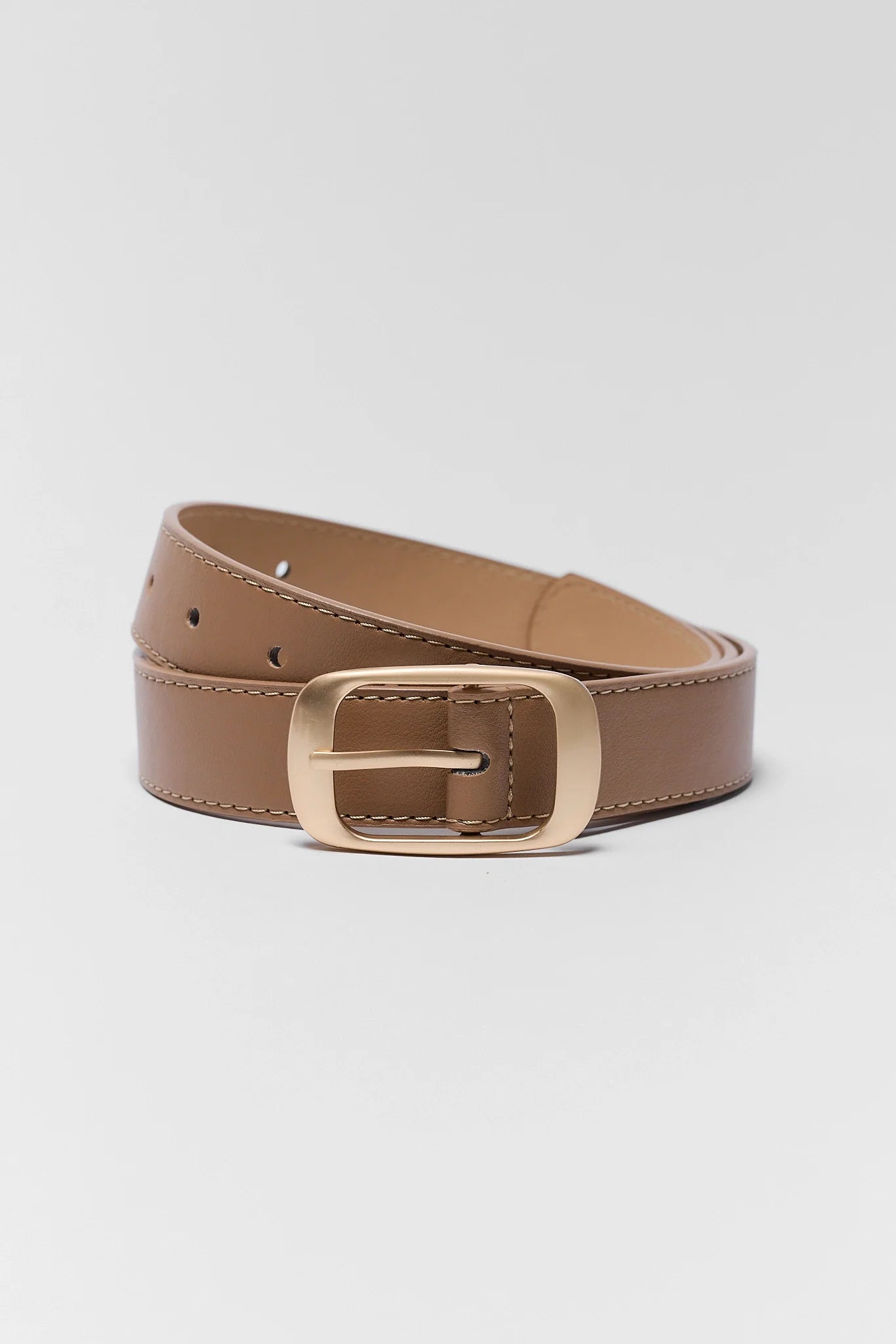 Tan faux leather belt with brushed gold buckle, coiled flat lay on gray background | Avara