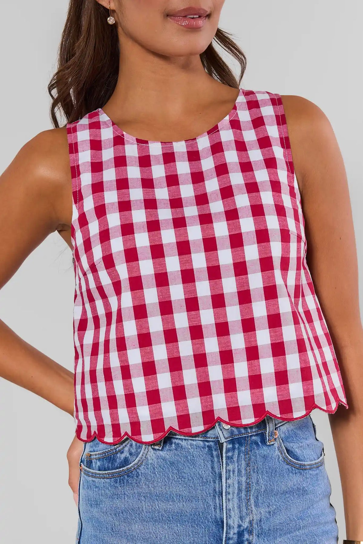 Close-up of red and white gingham tank top with scalloped hem detail, paired with blue jeans | Avara