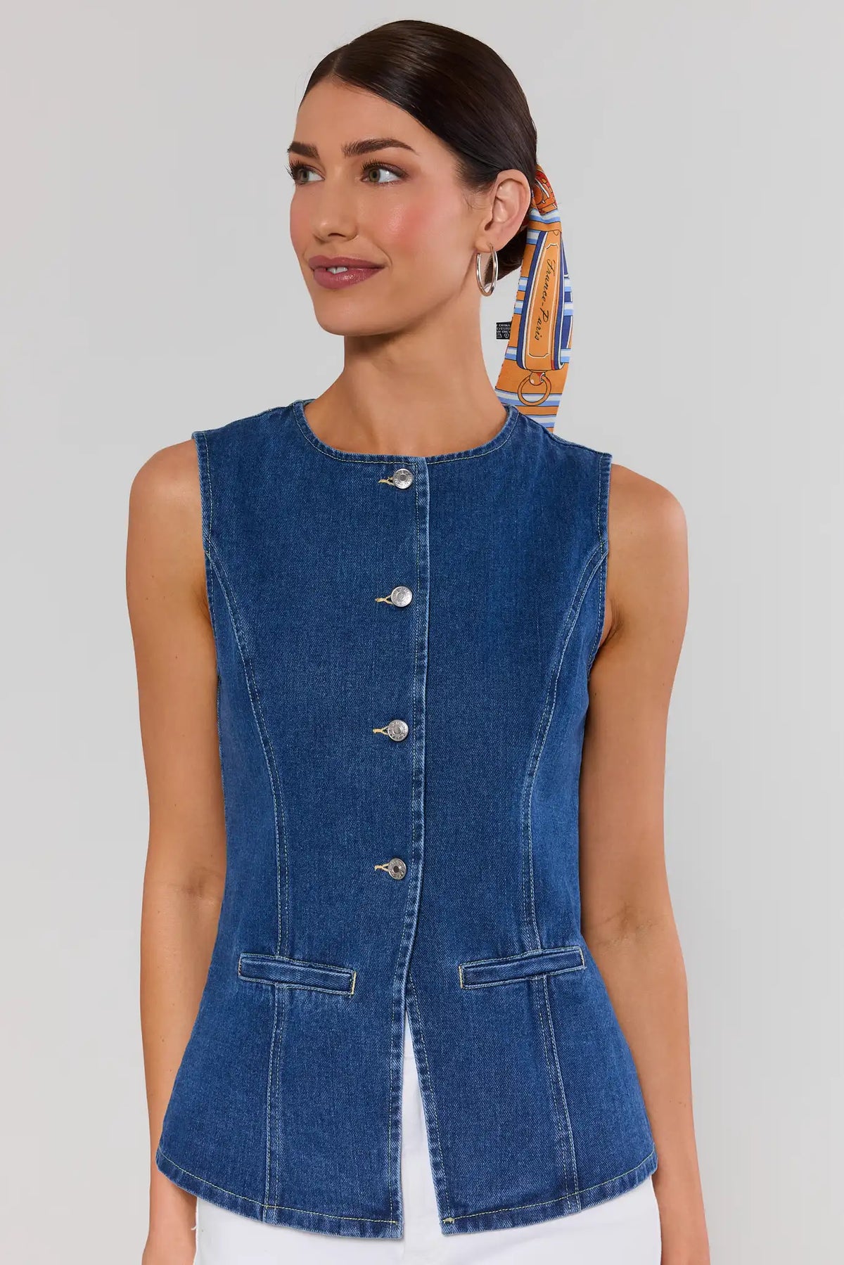 Woman wearing a blue denim vest on a plain background with hair scarf
