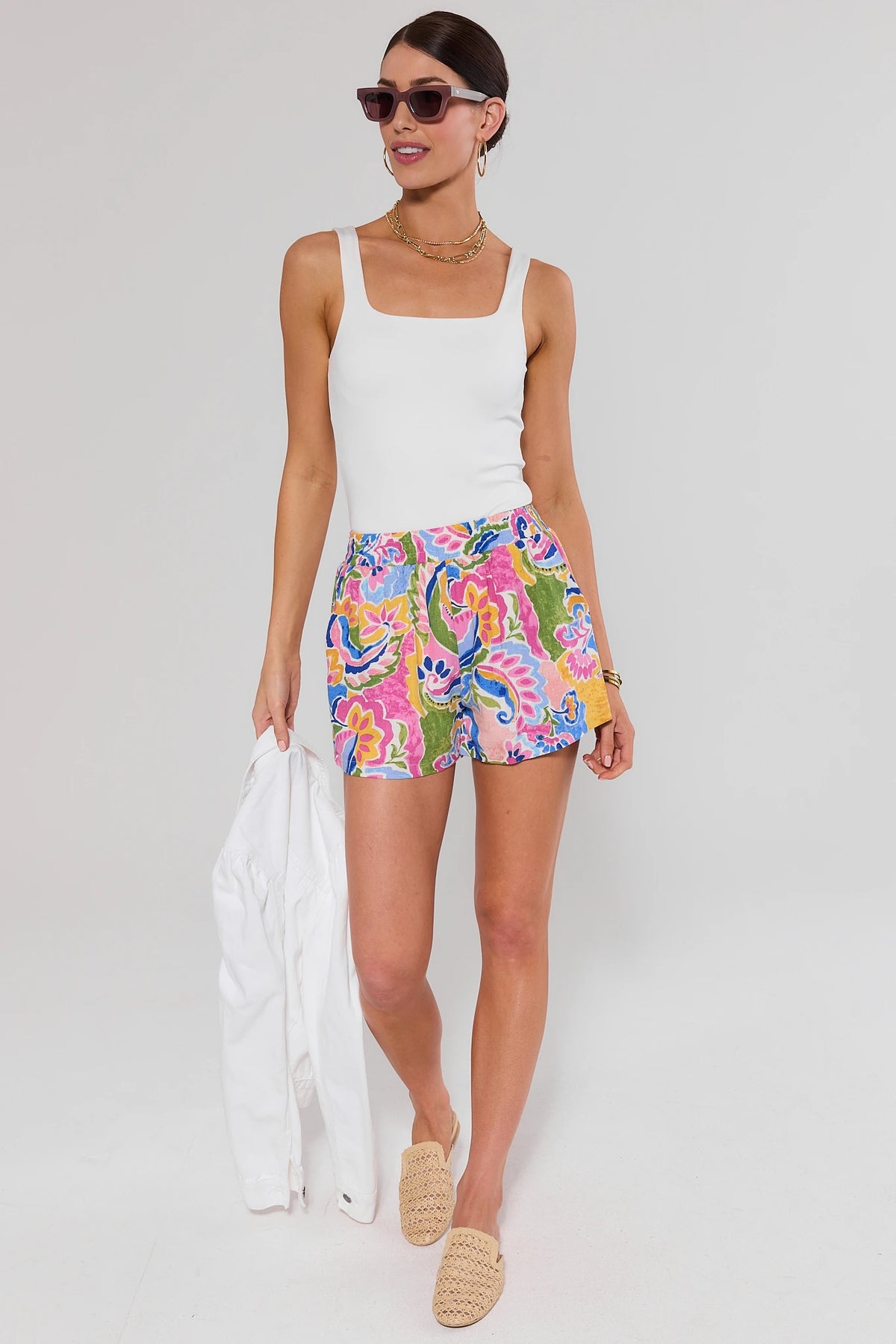 Woman standing wearing colorful shorts and a white top on a plain background