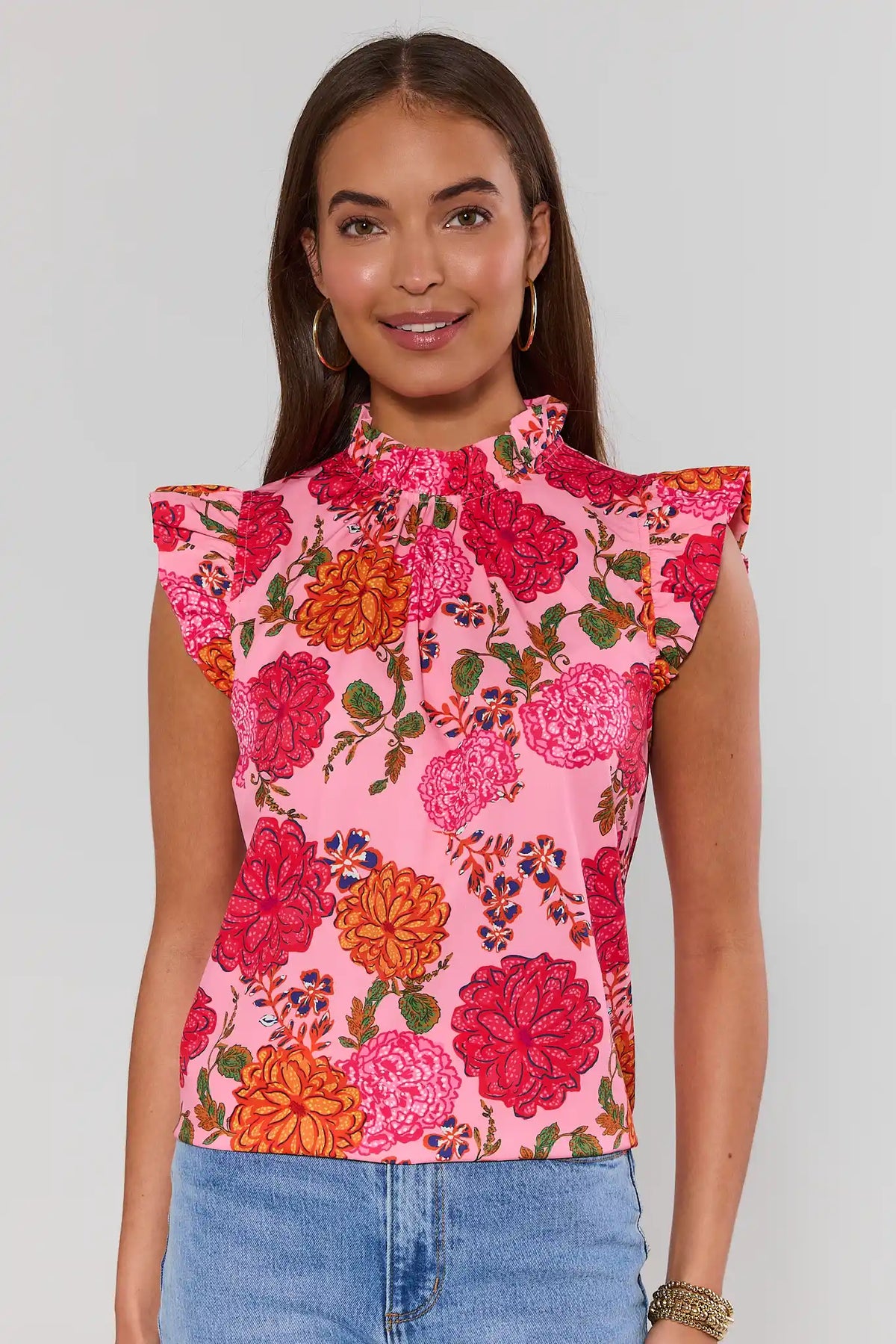 Woman standing wearing a pink floral top with a plain background 