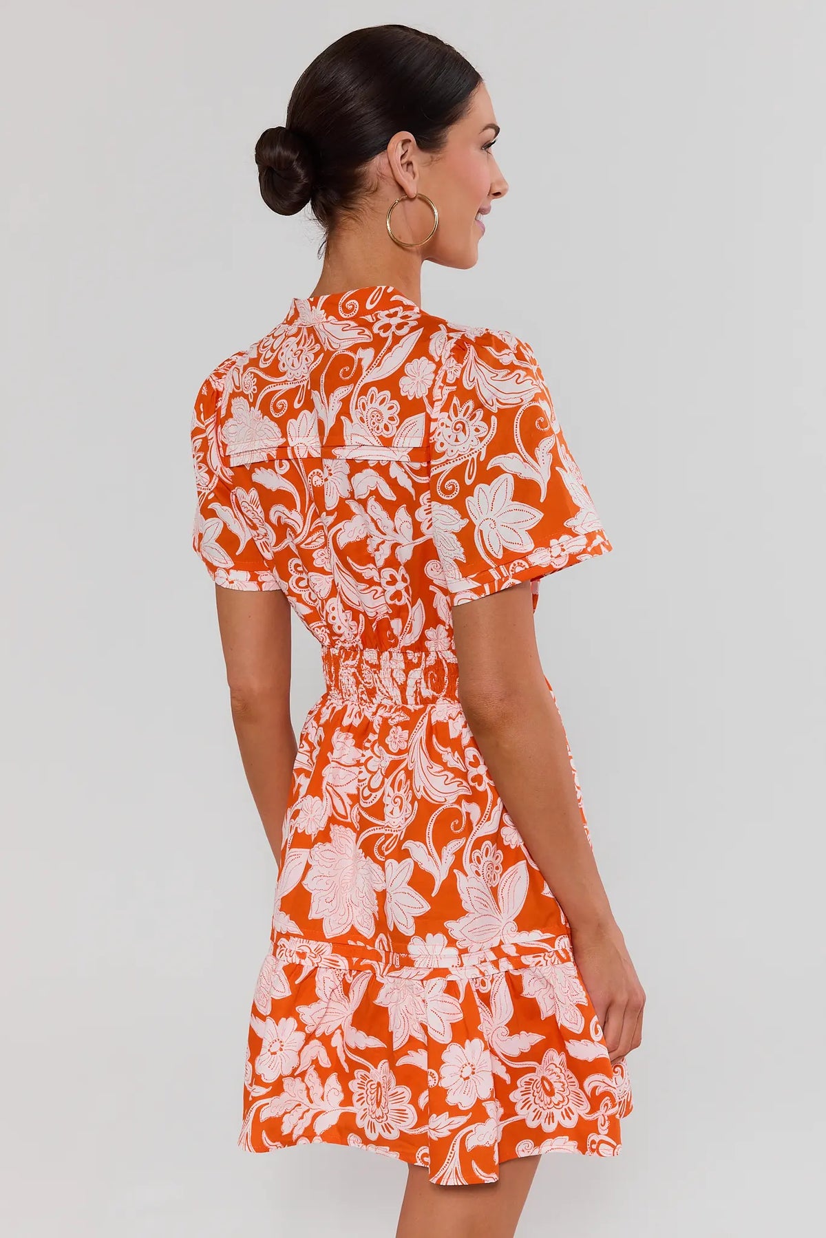 Woman wearing an orange and white floral dress against a plain background standing