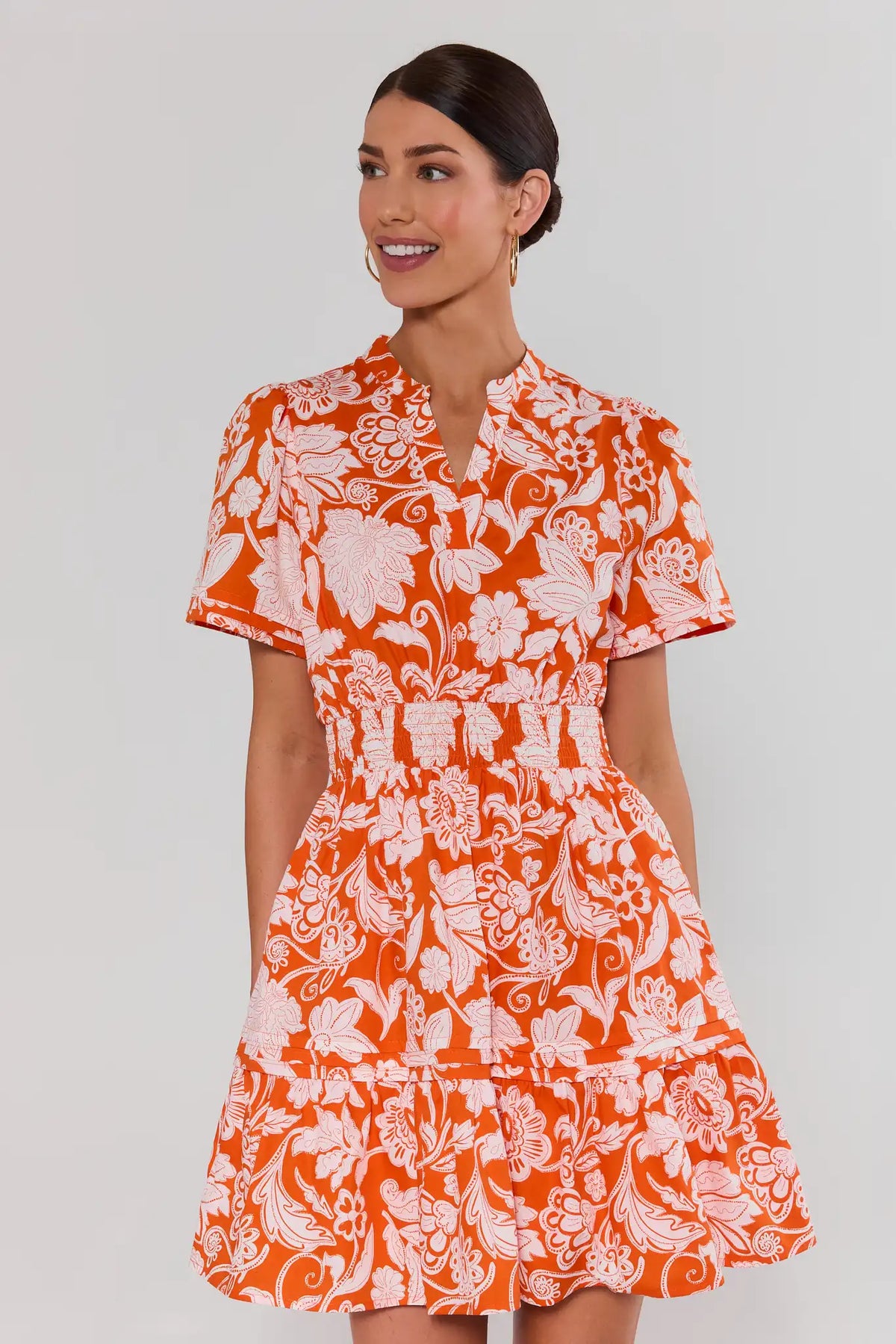 Woman wearing an orange and white floral isabella dress against a plain background