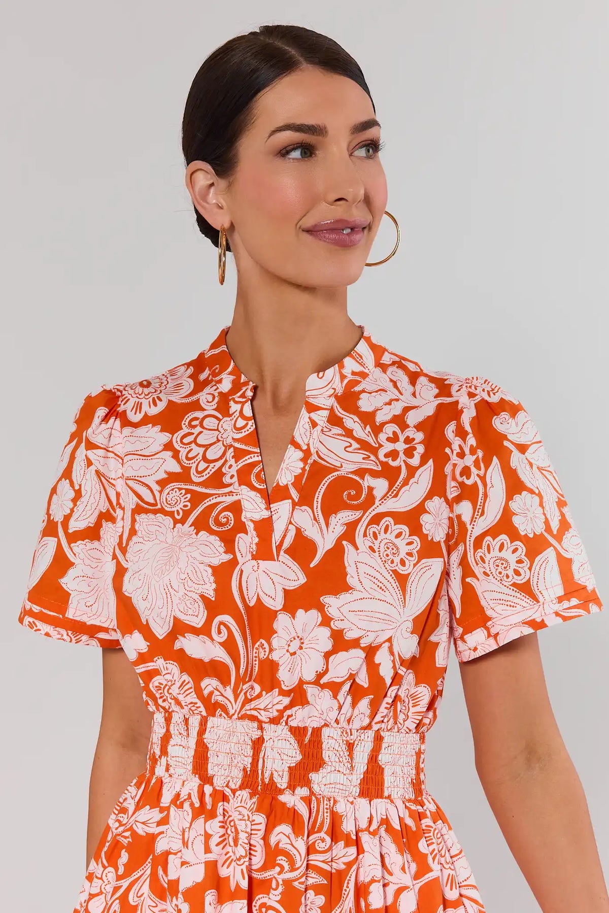 close up Woman wearing an orange floral dress against a plain background