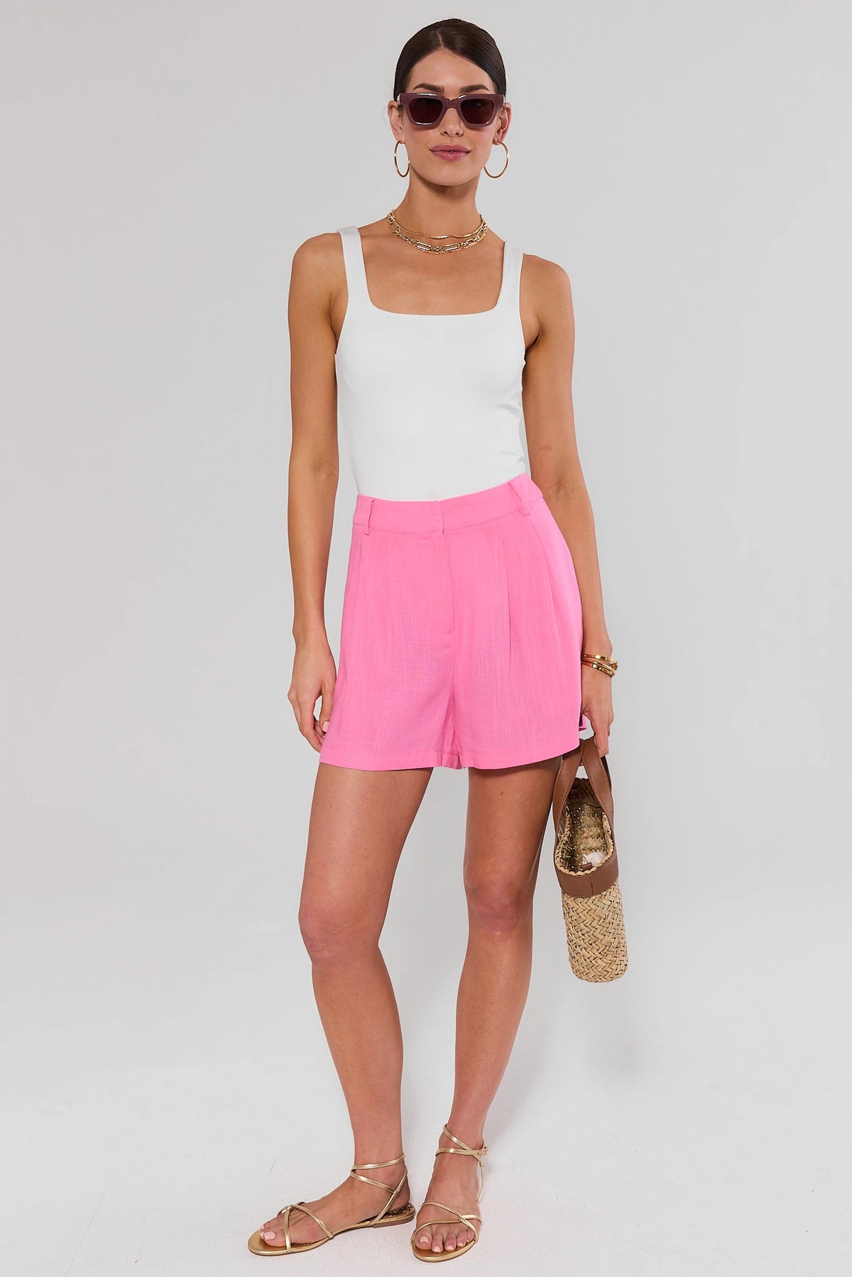Pink pleated trouser shorts styled with white tank and woven bag, full-length front view | Avara