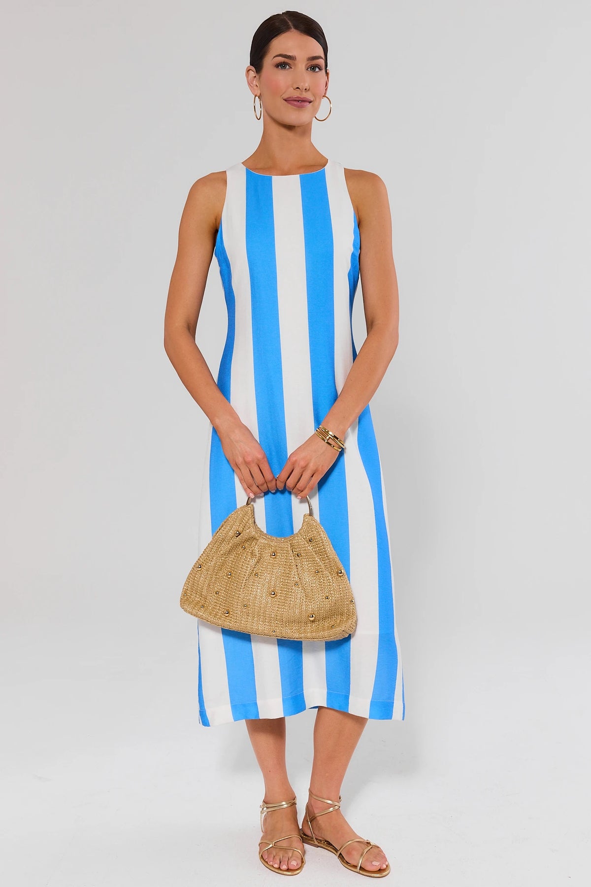 Woman wearing blue striped midi dress with gold sandals and woven bag, full-length styled look | Avara