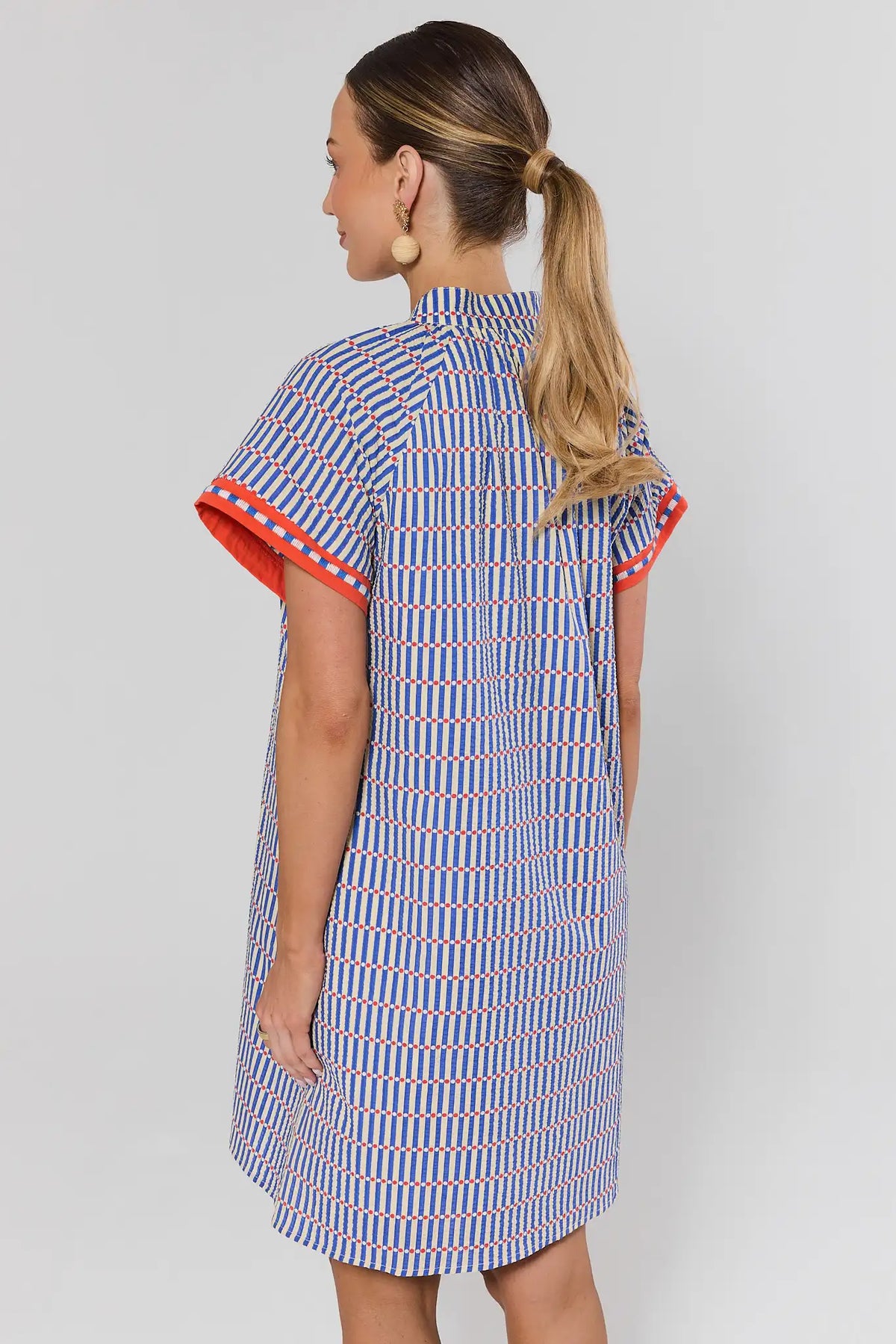 Woman wearing blue striped seersucker shift dress with red sleeve trim, back view | Avara