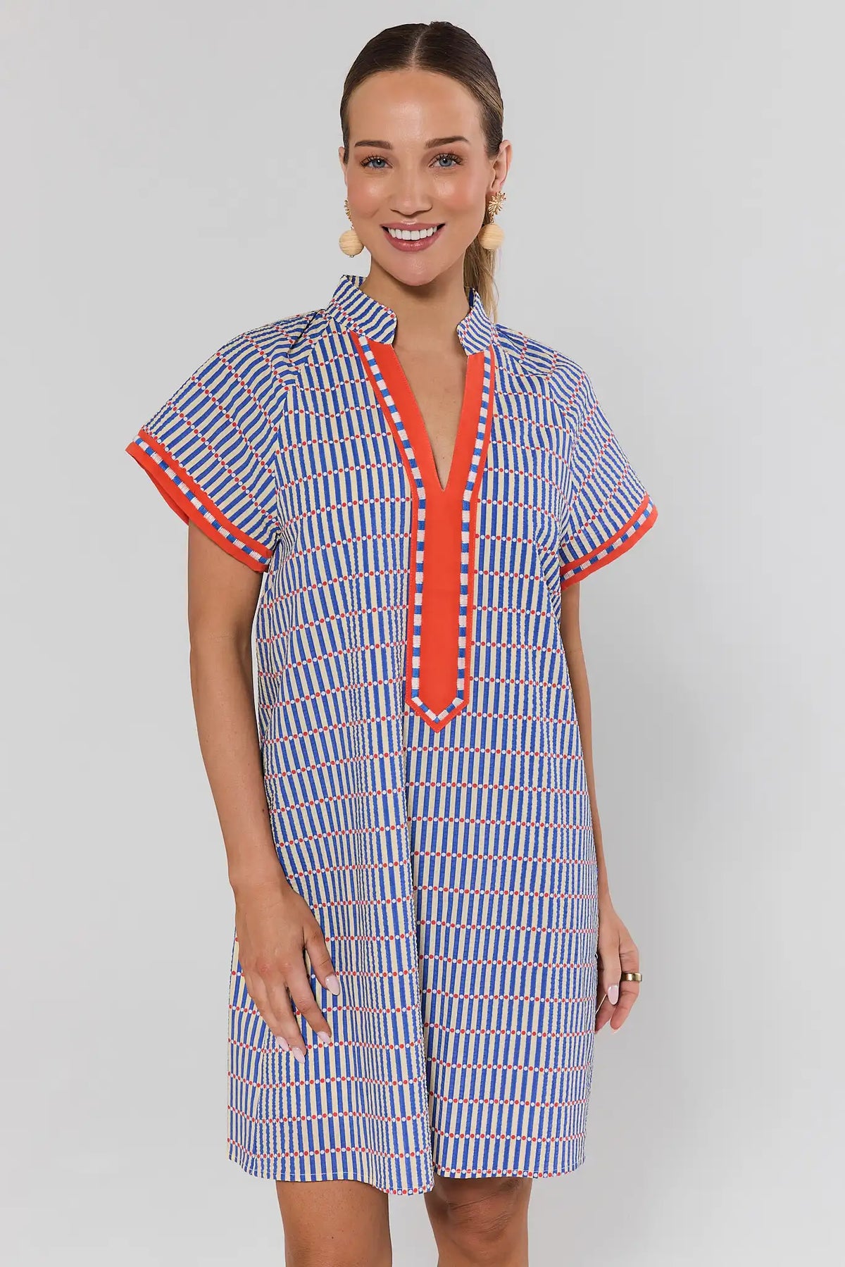 Woman wearing a blue striped seersucker short dress with red V-neckline trim, front view | Avara