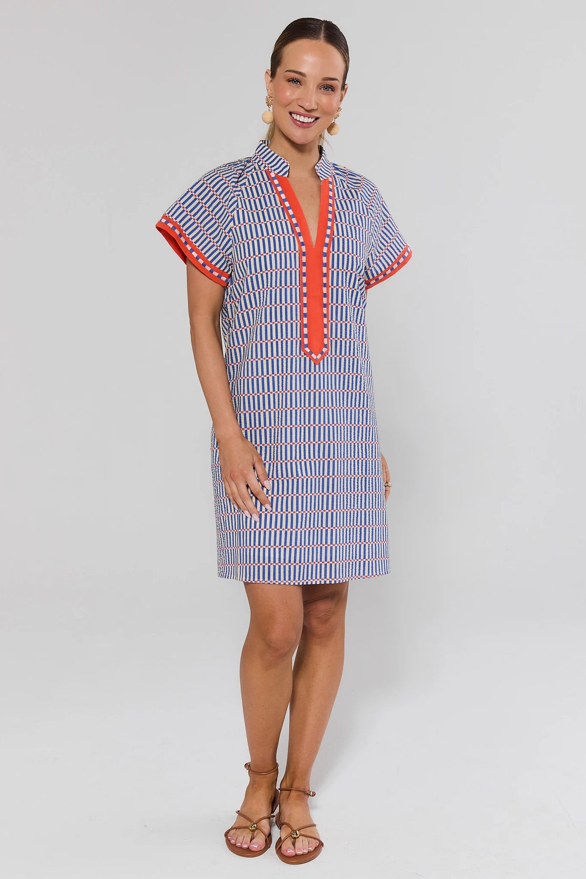 Woman wearing a blue striped seersucker shift dress with red trim, three-quarter view with sandals | Avara