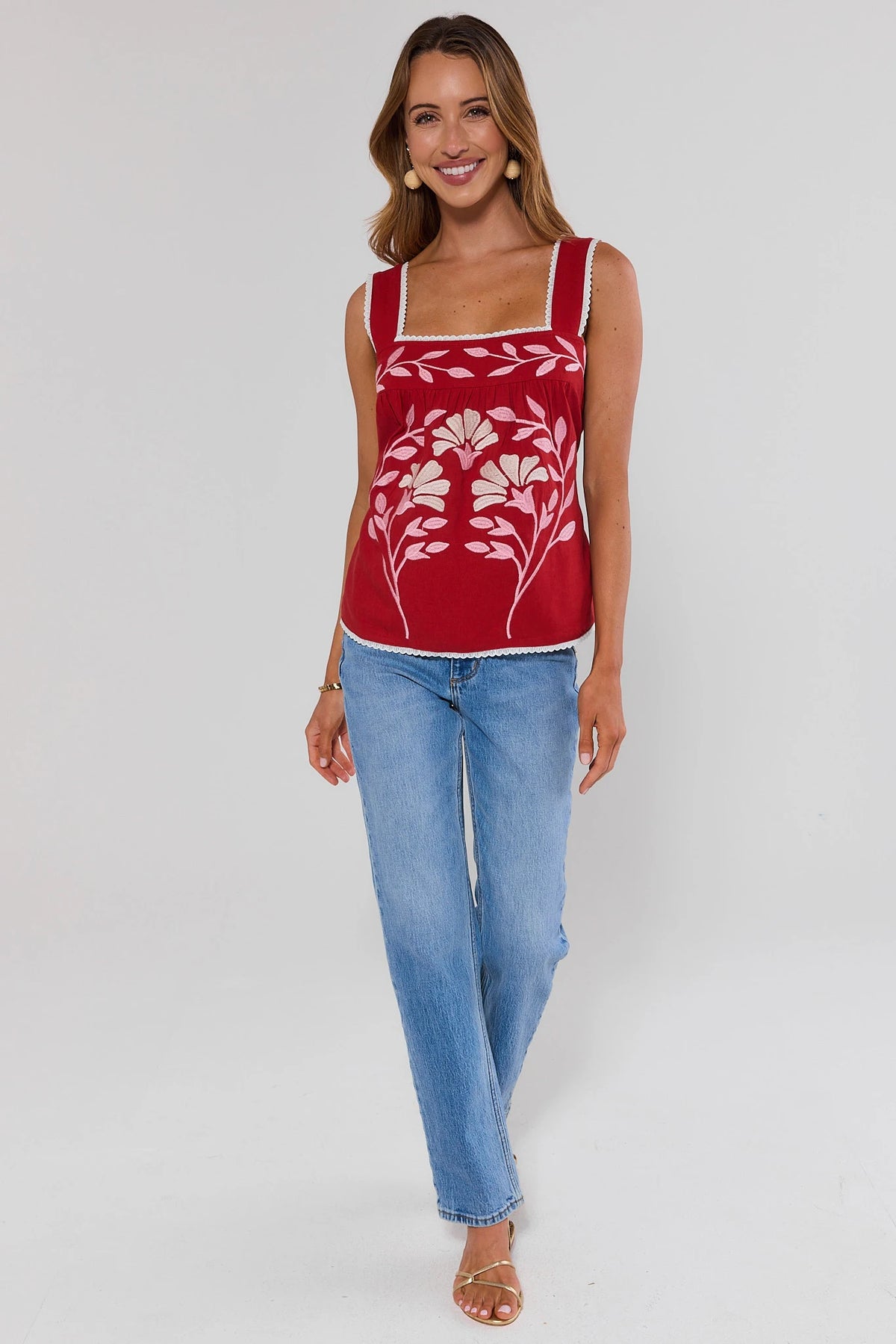 Woman wearing a red tank top with floral design and blue jeans on a white background