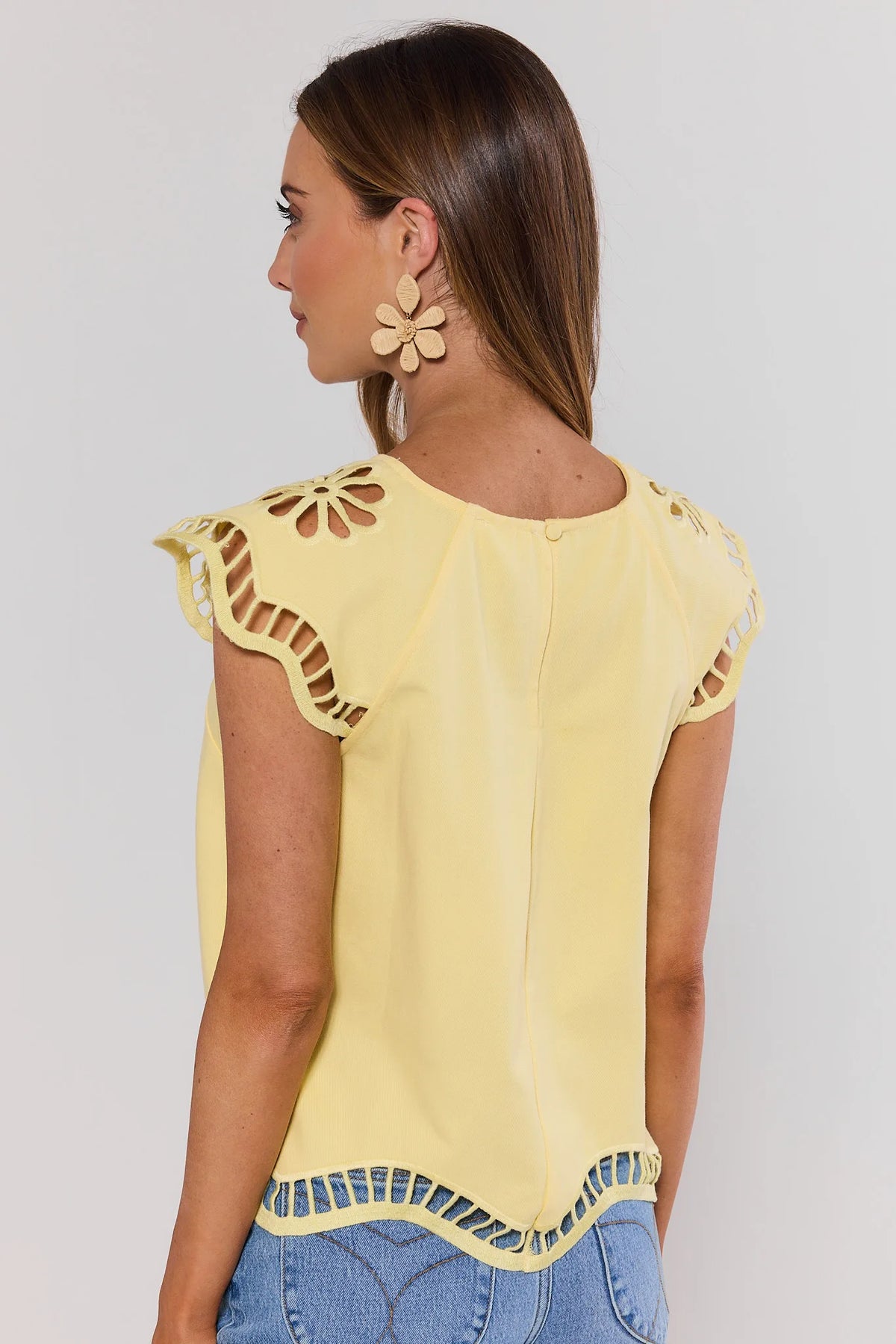 Woman wearing a yellow top with cut-out details on a plain background standing