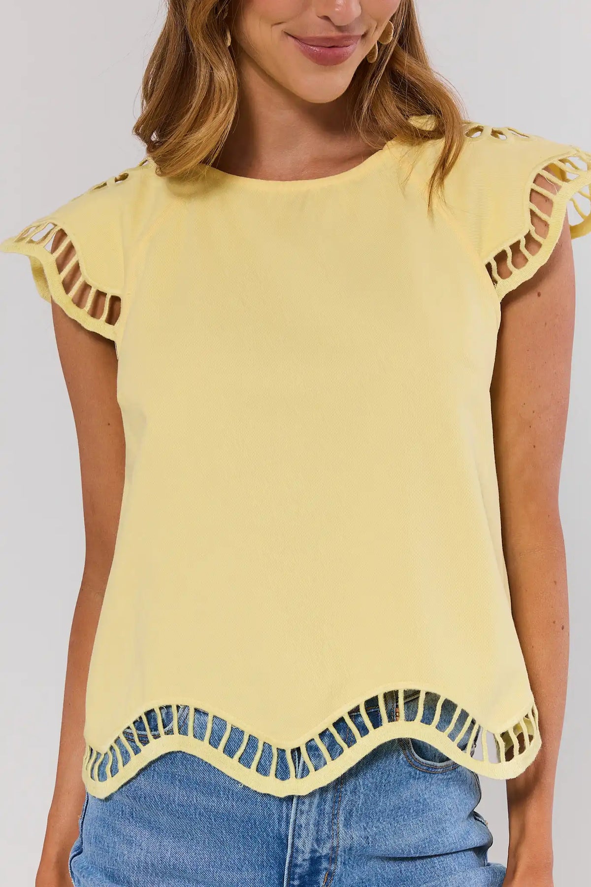 close up Woman wearing a yellow top with cut-out shoulders and hem, standing against a plain background.