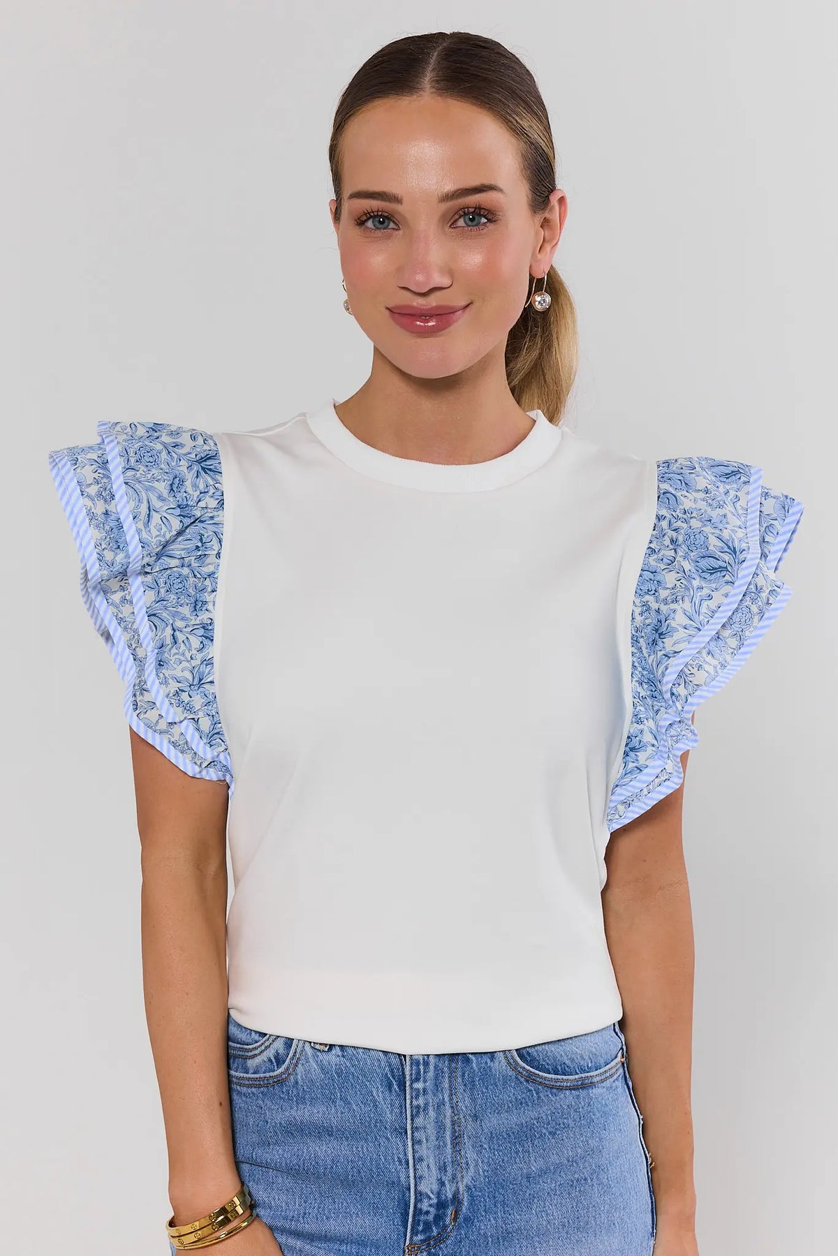 Woman wearing a white top with blue floral sleeves against a plain background