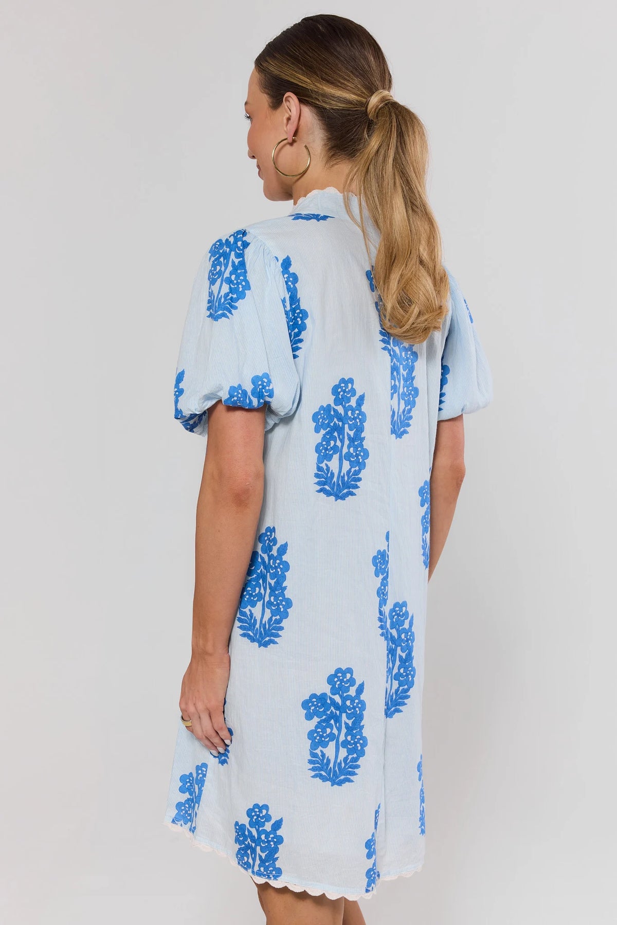 Woman standing wearing a white dress with blue floral patterns on a plain background