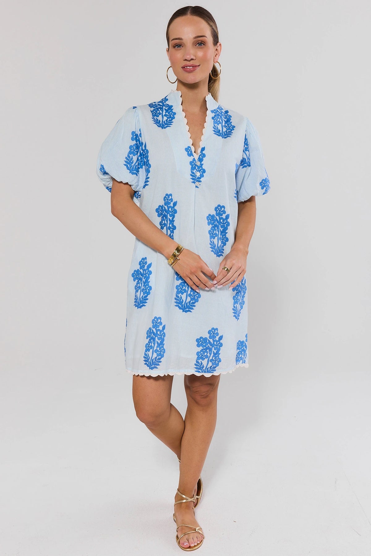 Woman wearing a light blue dress with blue floral patterns and sandals on a white background