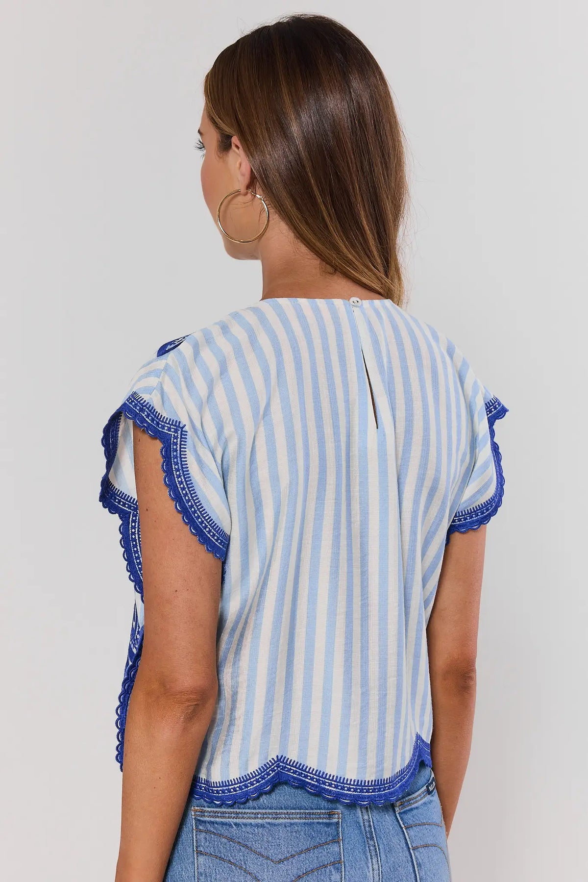 Woman wearing a blue and white striped shirt with ruffled sleeves on a plain background standing