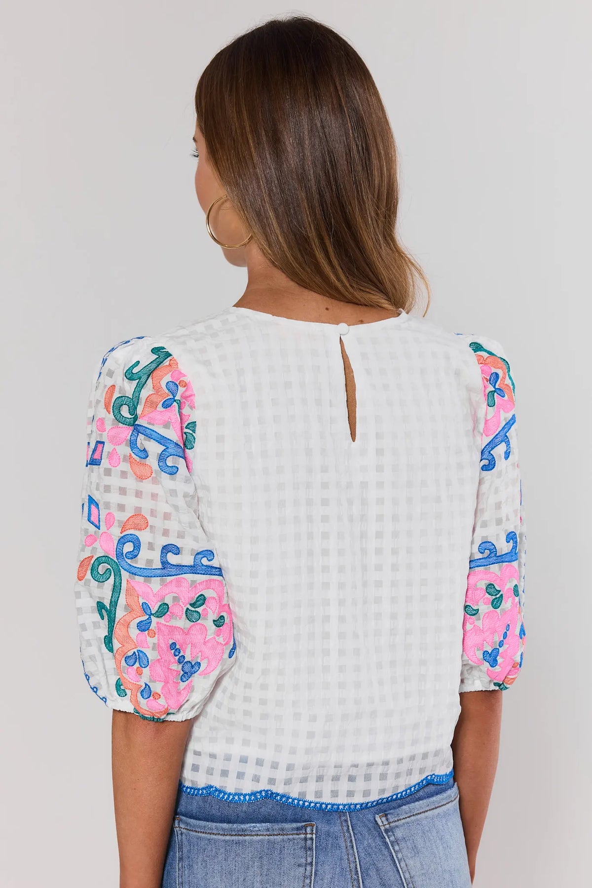 Woman wearing a white blouse with colorful floral patterns on sleeves against a plain background