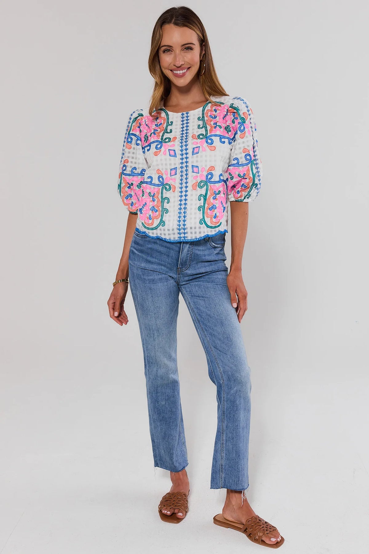 Woman wearing a colorful embroidered blouse and blue jeans on a white background