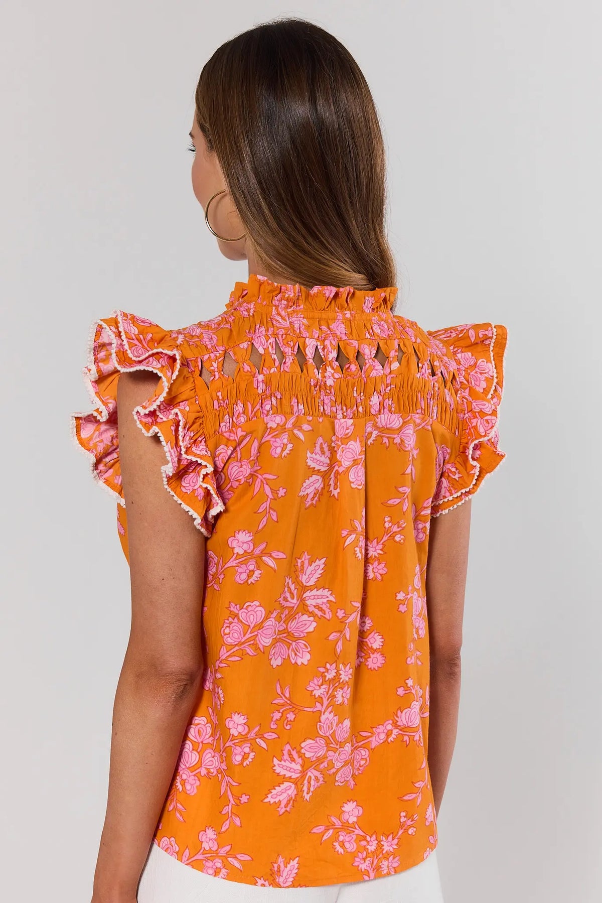 Woman standing wearing an orange floral blouse with ruffled sleeves on a plain background