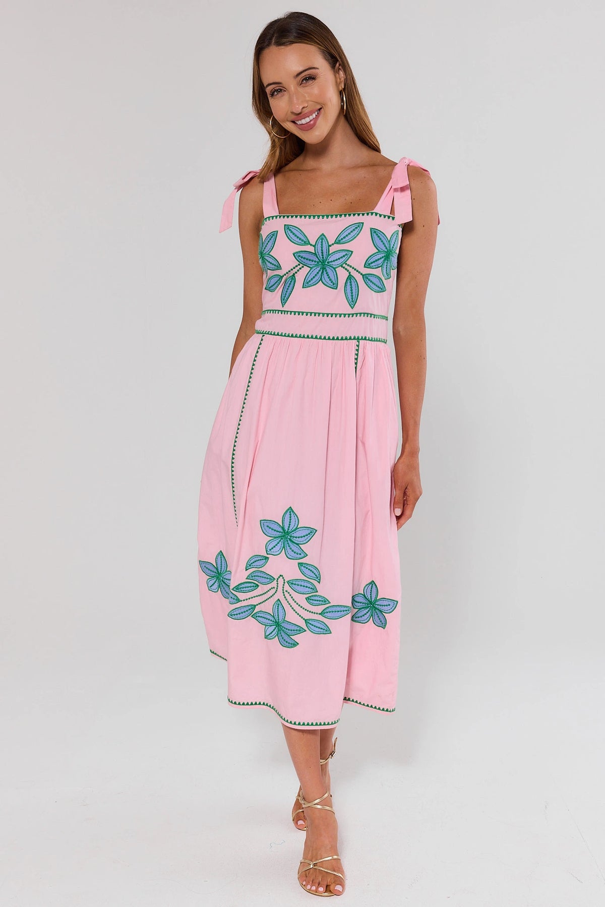 Woman standing wearing a pink dress with floral embroidery on a white background
