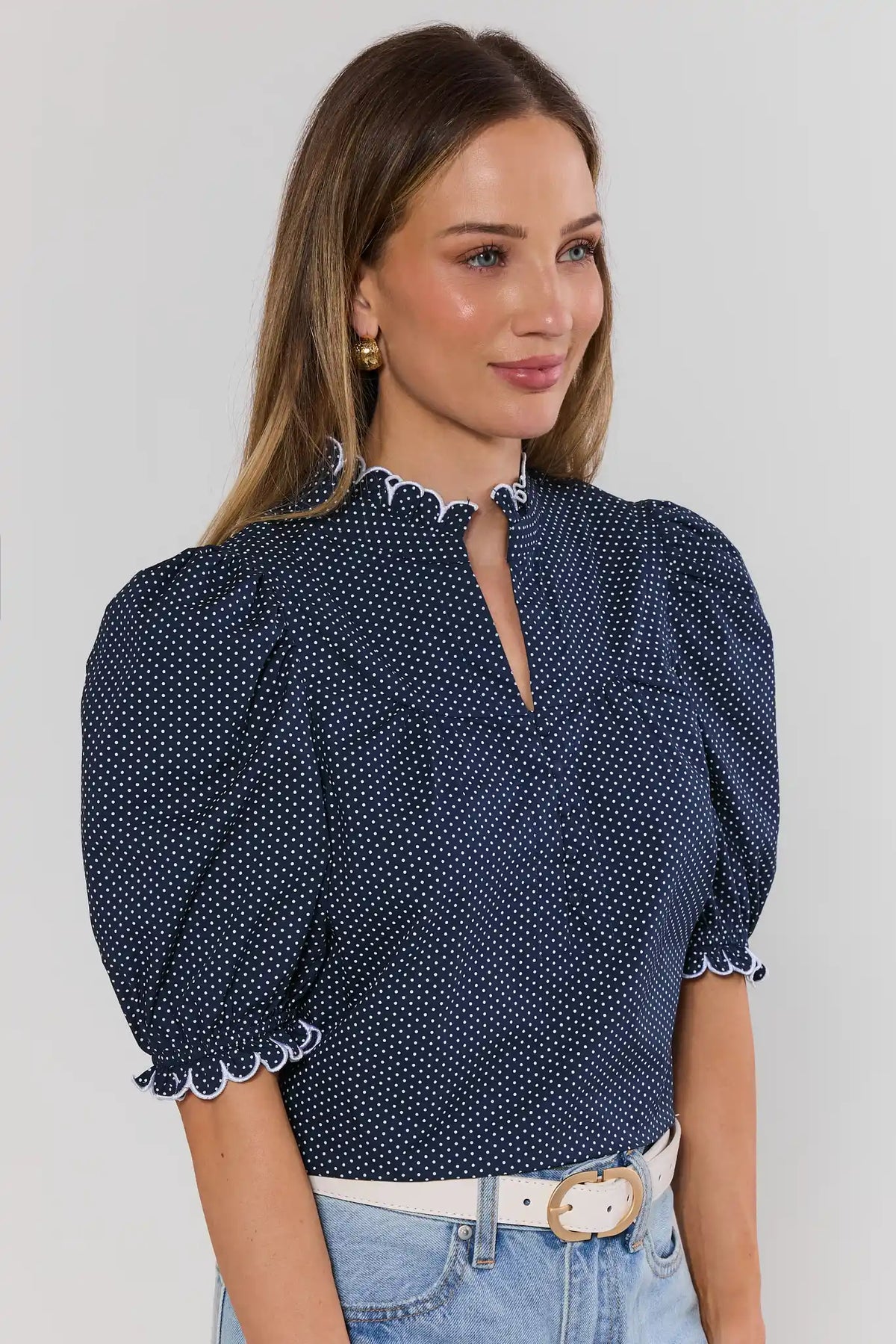Navy blue polka dot puff sleeve top with white scallop trim, paired with jeans - Three-Quarter View | Avara