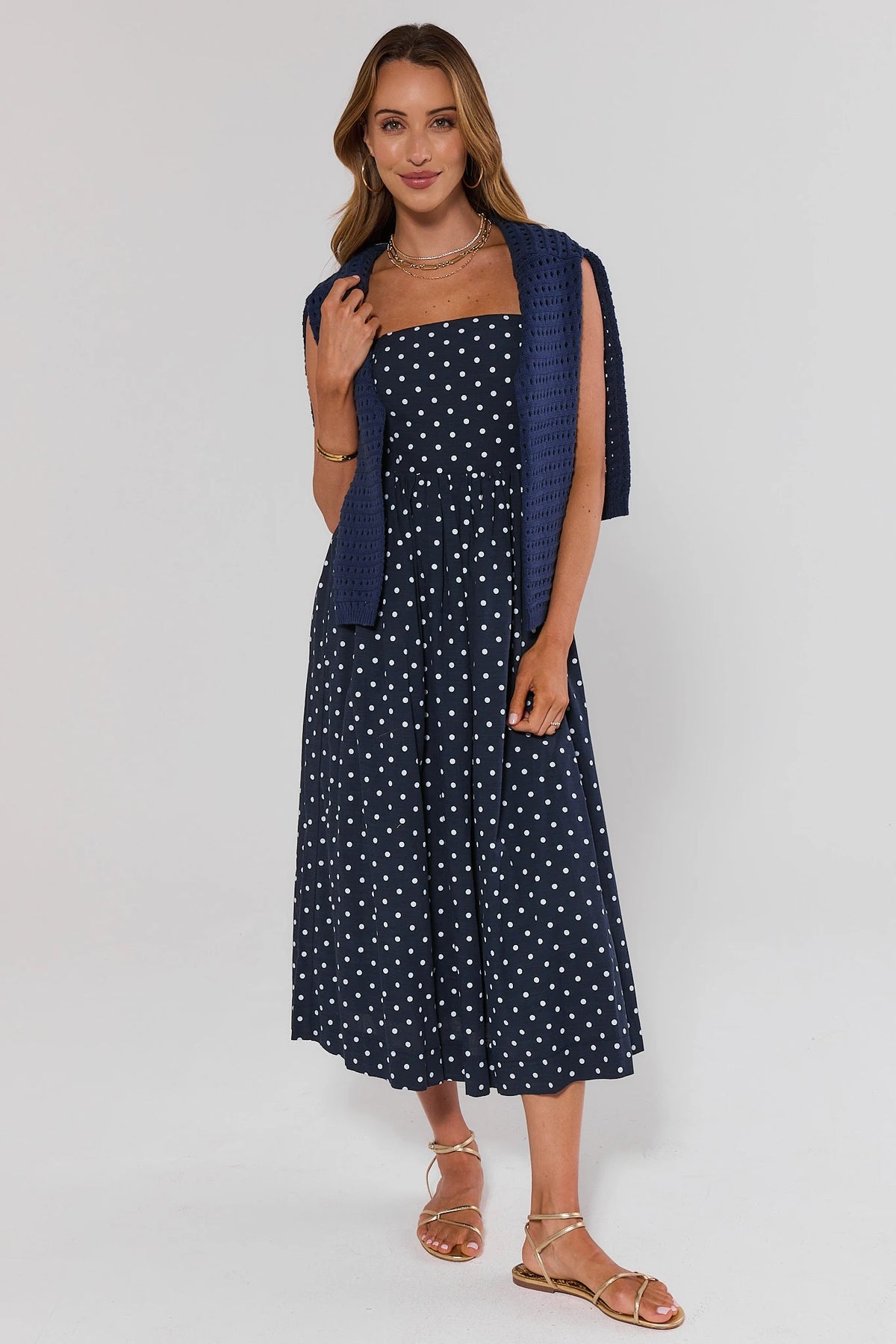 Navy blue polka dot midi dress styled with matching navy cardigan and gold sandals - Styled Look | Avara