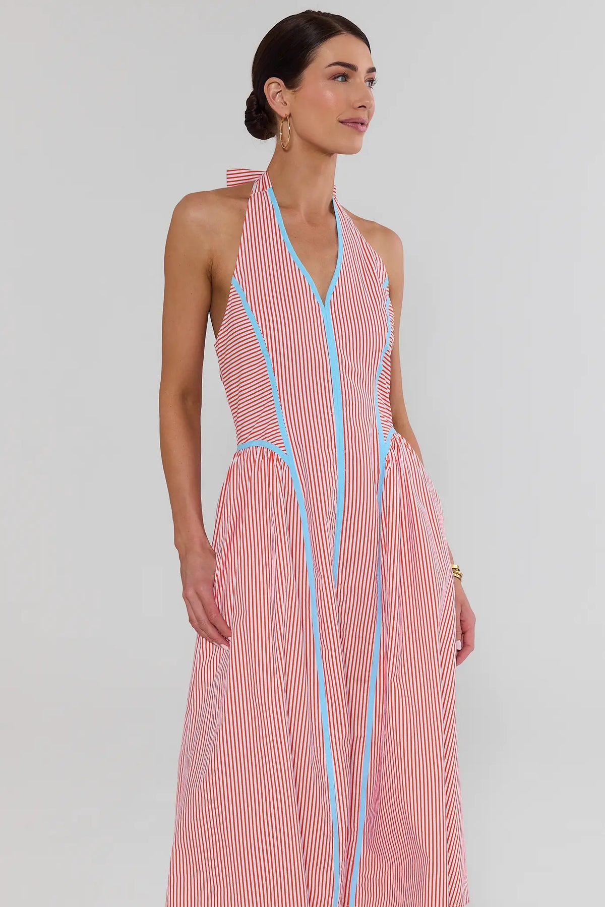 Woman wearing a pink and blue striped dress against a white background stand