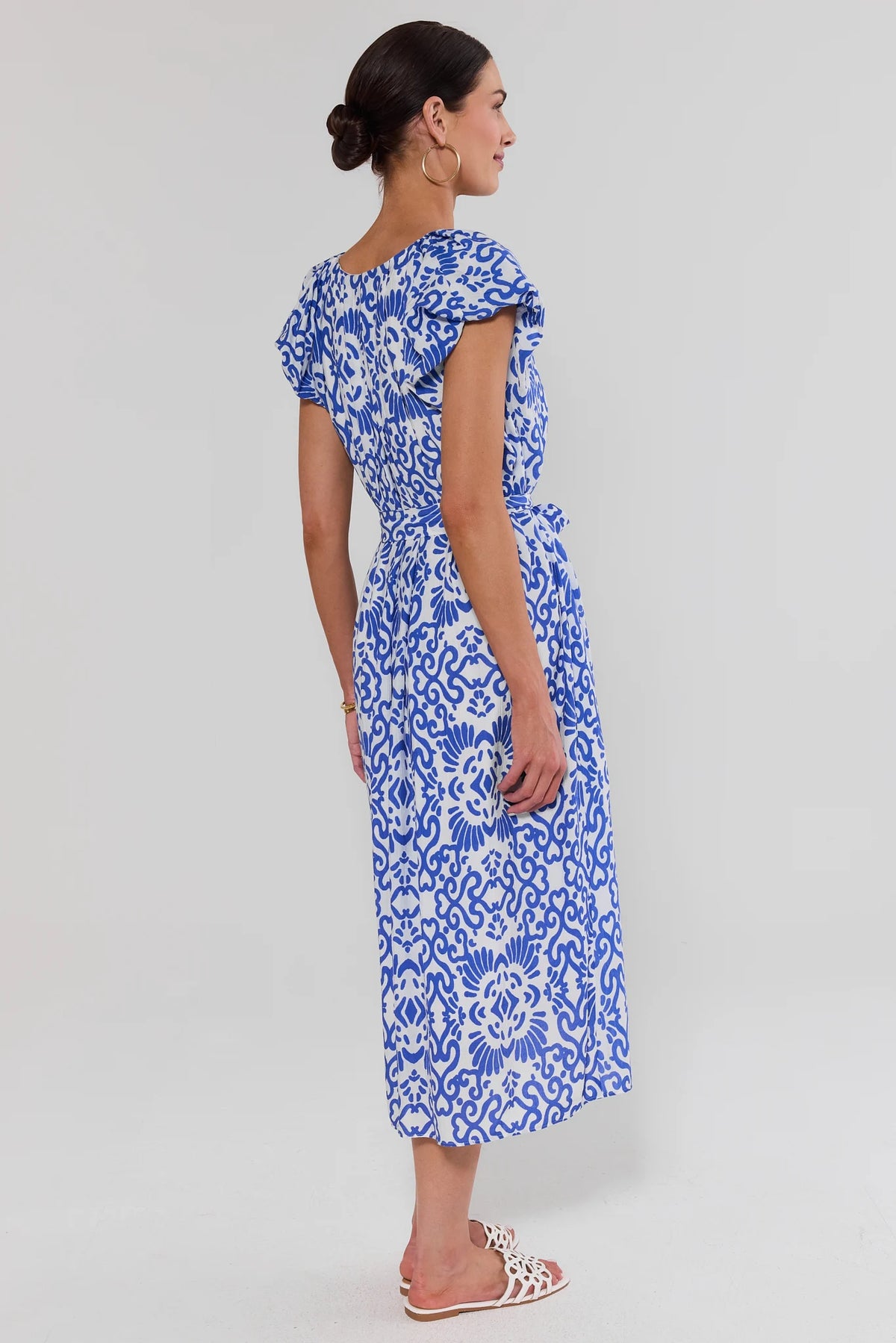 Blue printed modest midi dress showing tie waist and flowy skirt with white sandals - Back View | Avara