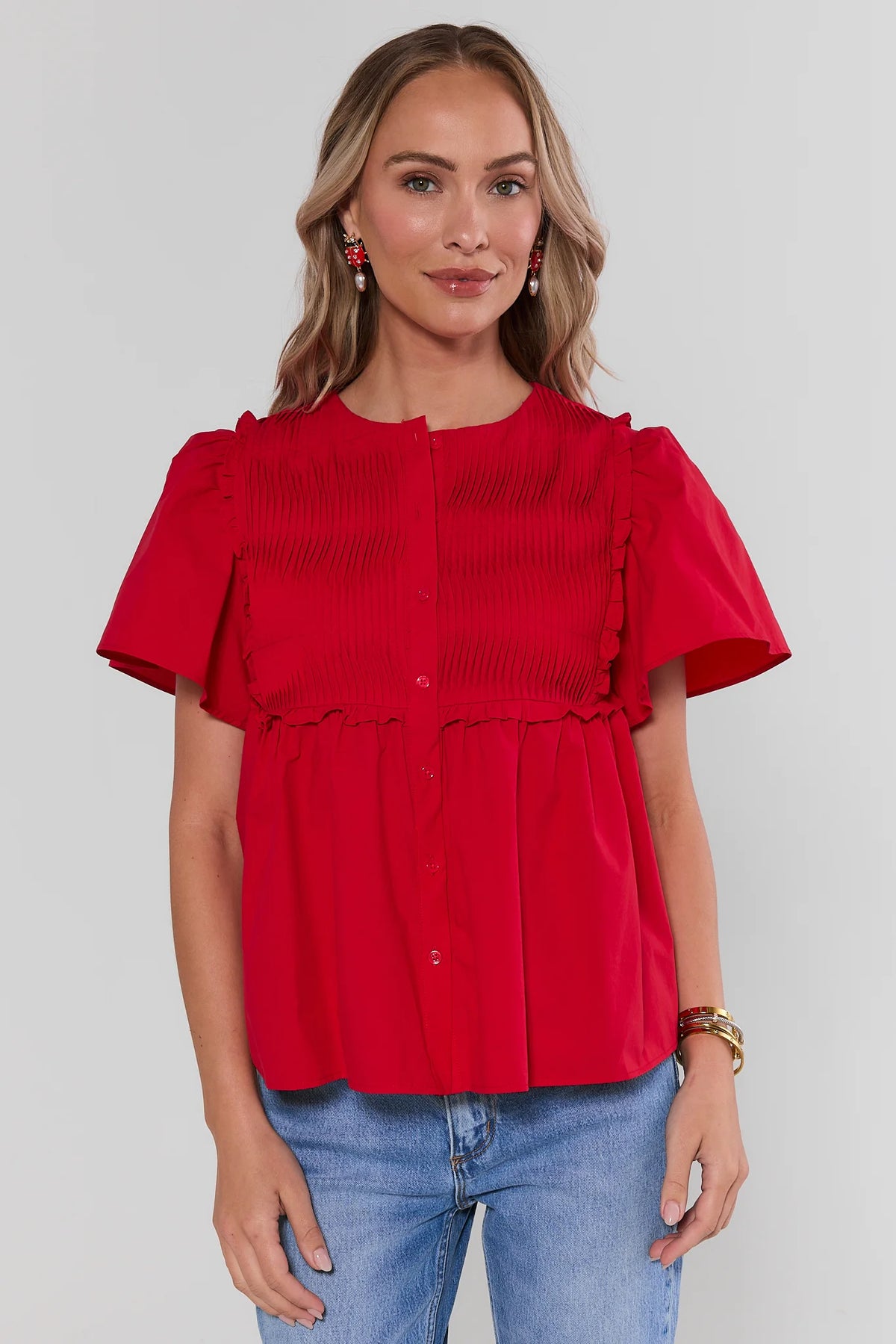 Red micro-pleated peplum top with flutter sleeves and button front, styled with blue jeans - Front View | Avara