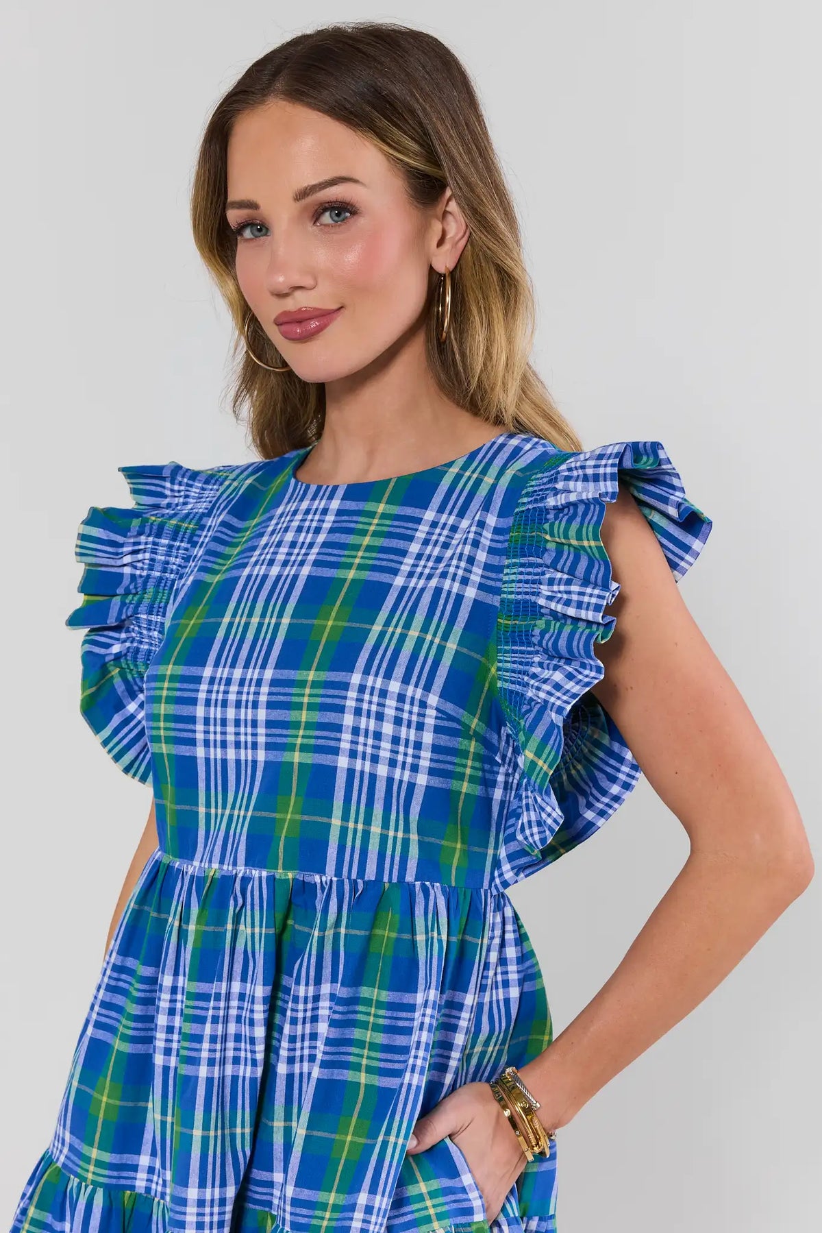 Blue plaid flutter sleeve dress close-up showing smocked ruffle detail and tiered bodice on model | Avara