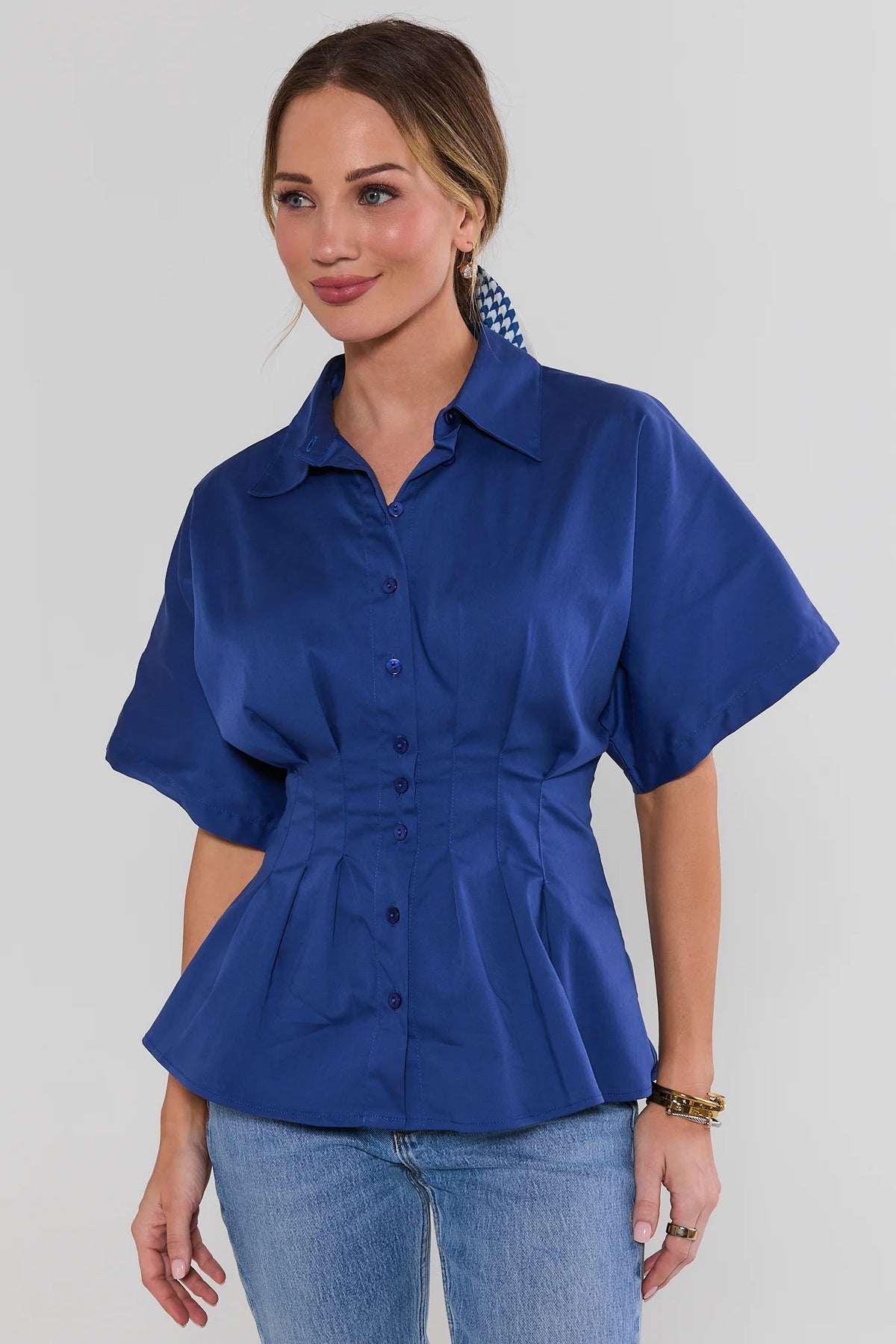 Woman wearing blue pleated button up peplum top with short sleeves, front view on model | Avara
