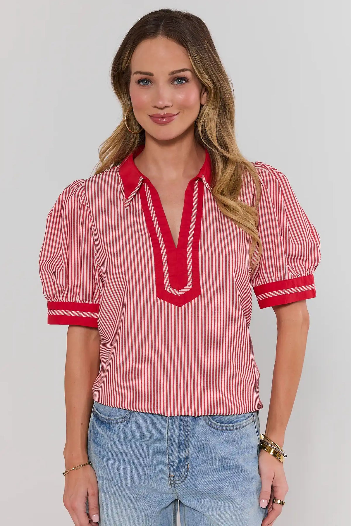 Woman wearing a red and white striped blouse with blue jeans on a plain background