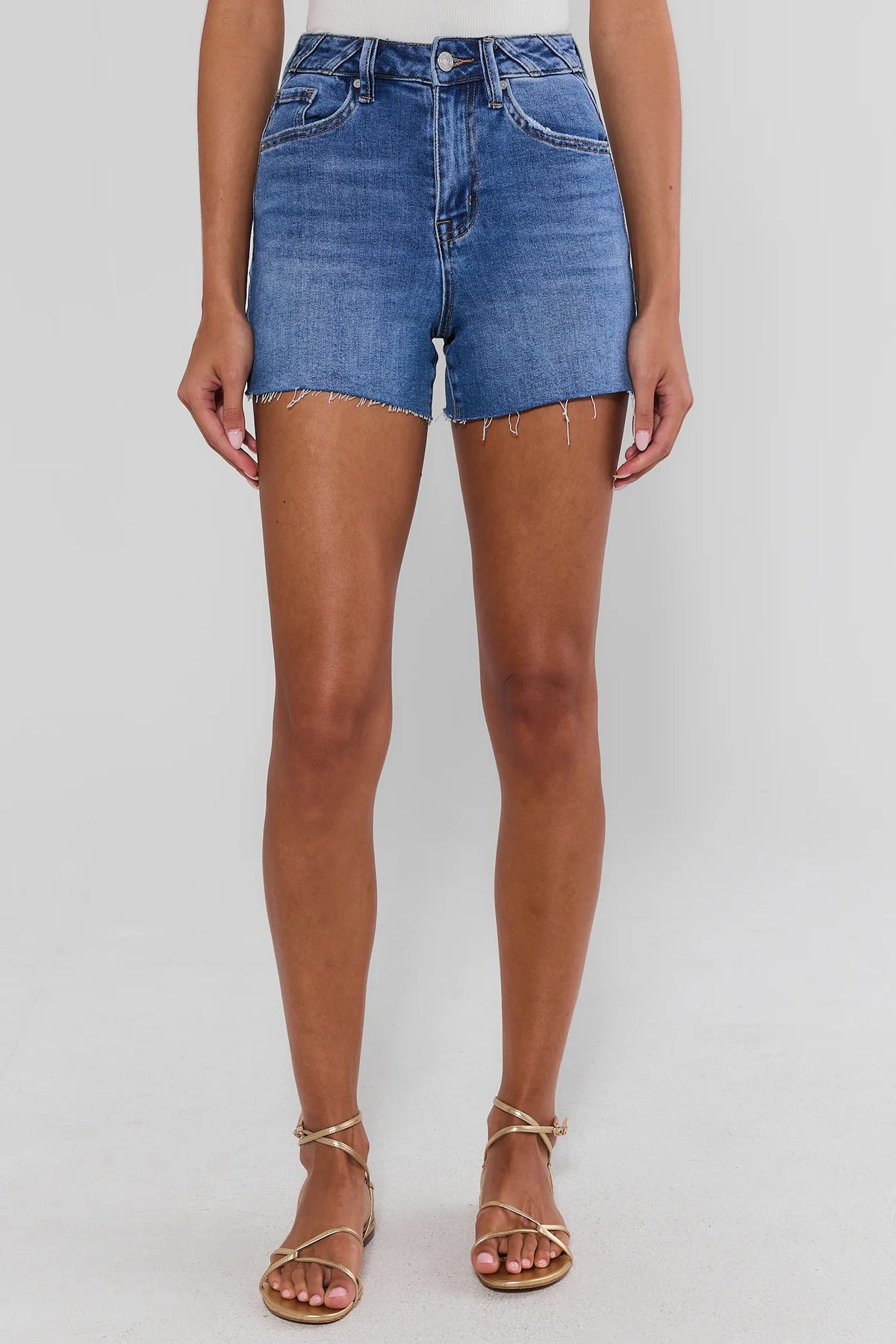 Woman standing in medium wash raw hem jean shorts with gold sandals, full-length front view | Avara