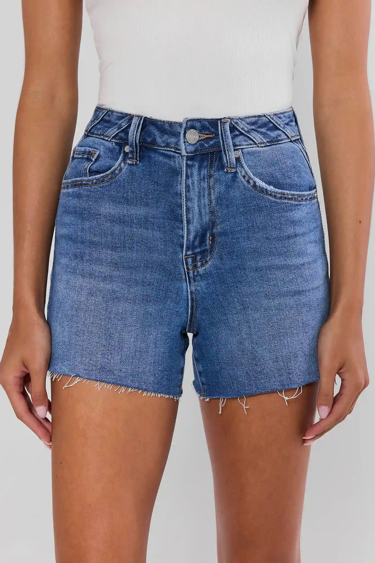 Medium wash raw hem jean shorts on model, close-up front view showing frayed hem detail | Avara