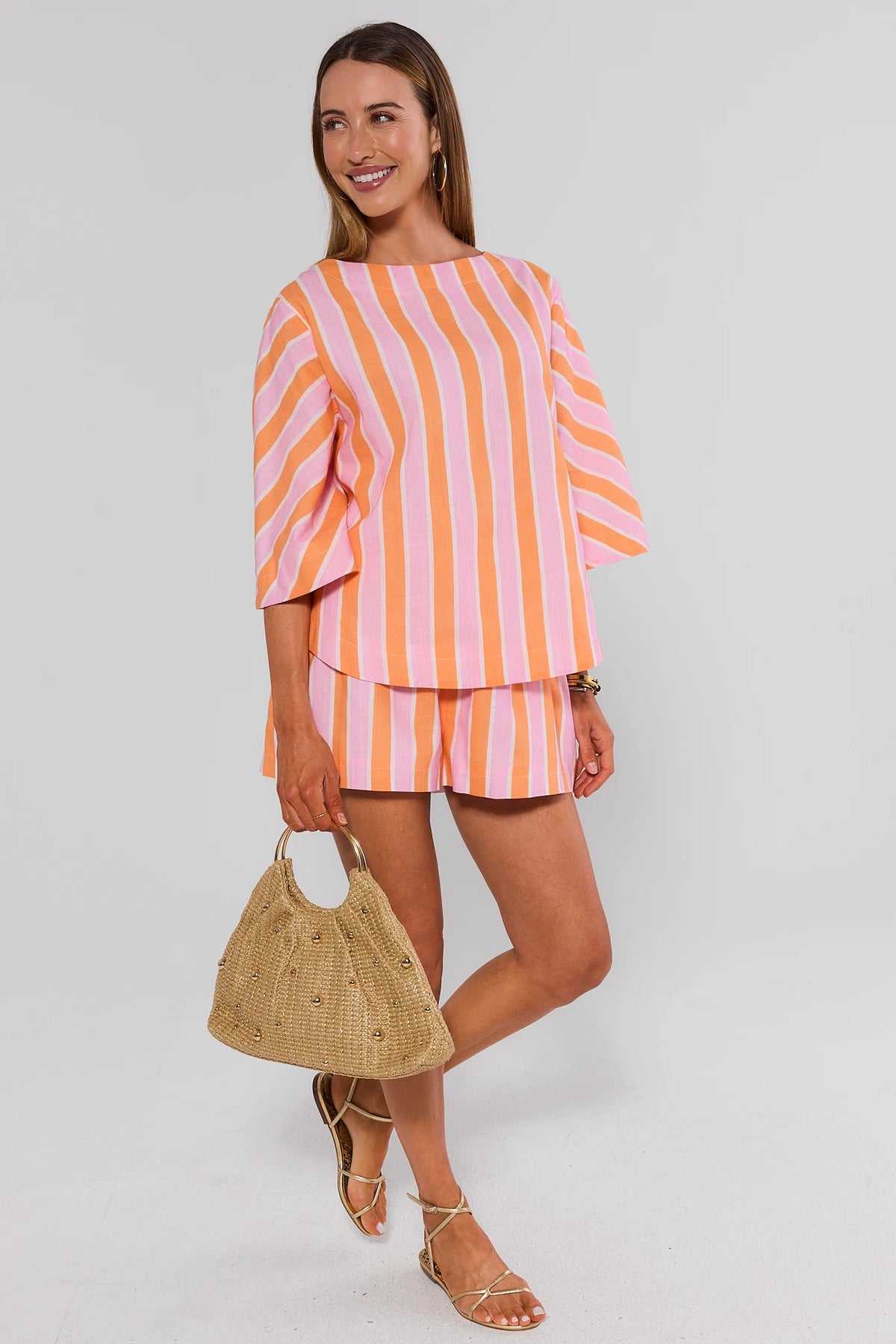 Woman wearing pink and orange striped matching shorts set with woven bag, full-length styled look | Avara