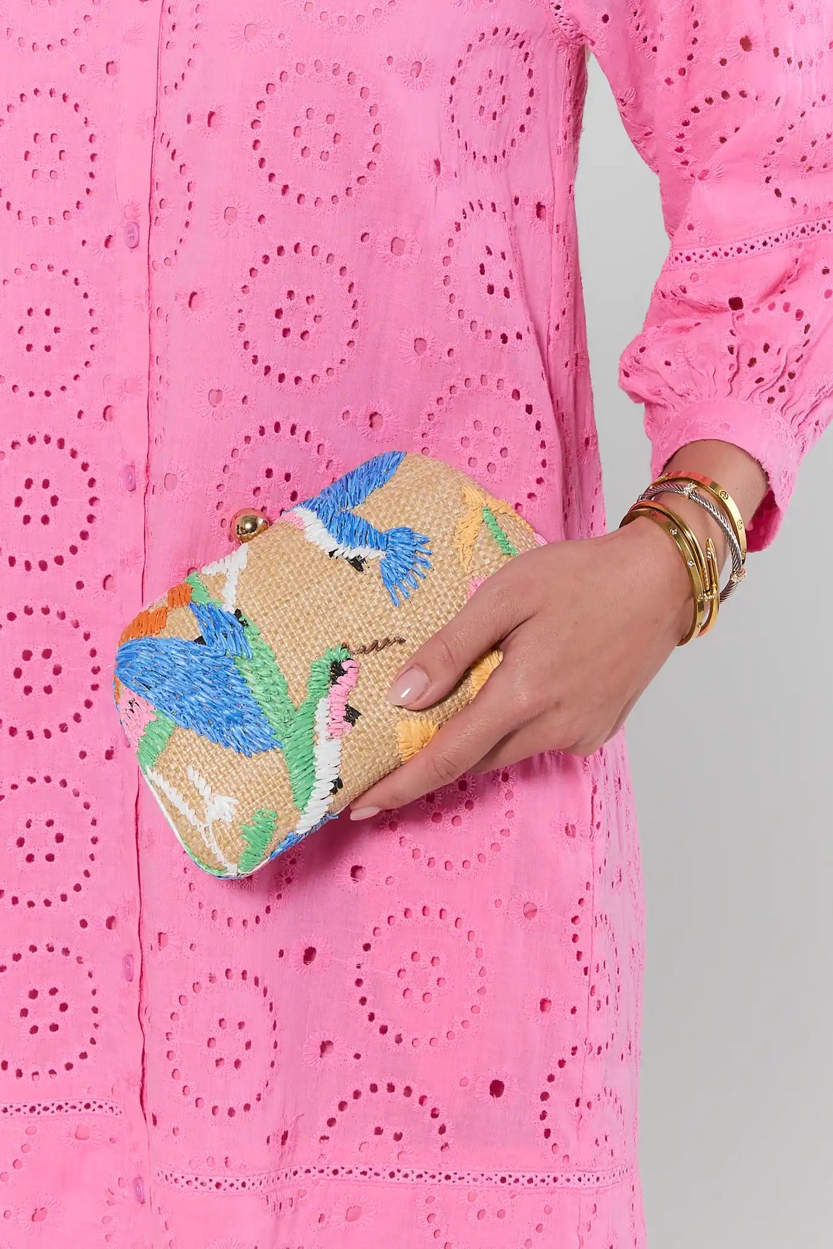 Person wearing a pink embroidered outfit holding a colorful beaded clutch.